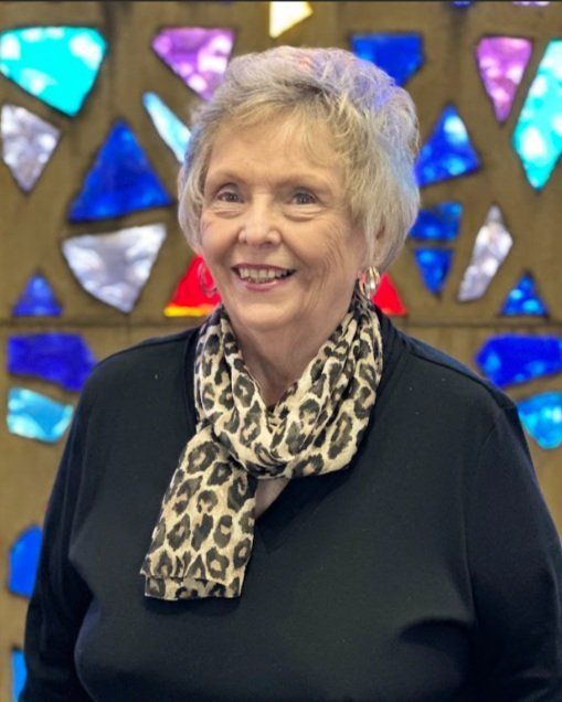 A woman wearing a leopard print scarf is smiling in front of a stained glass window.