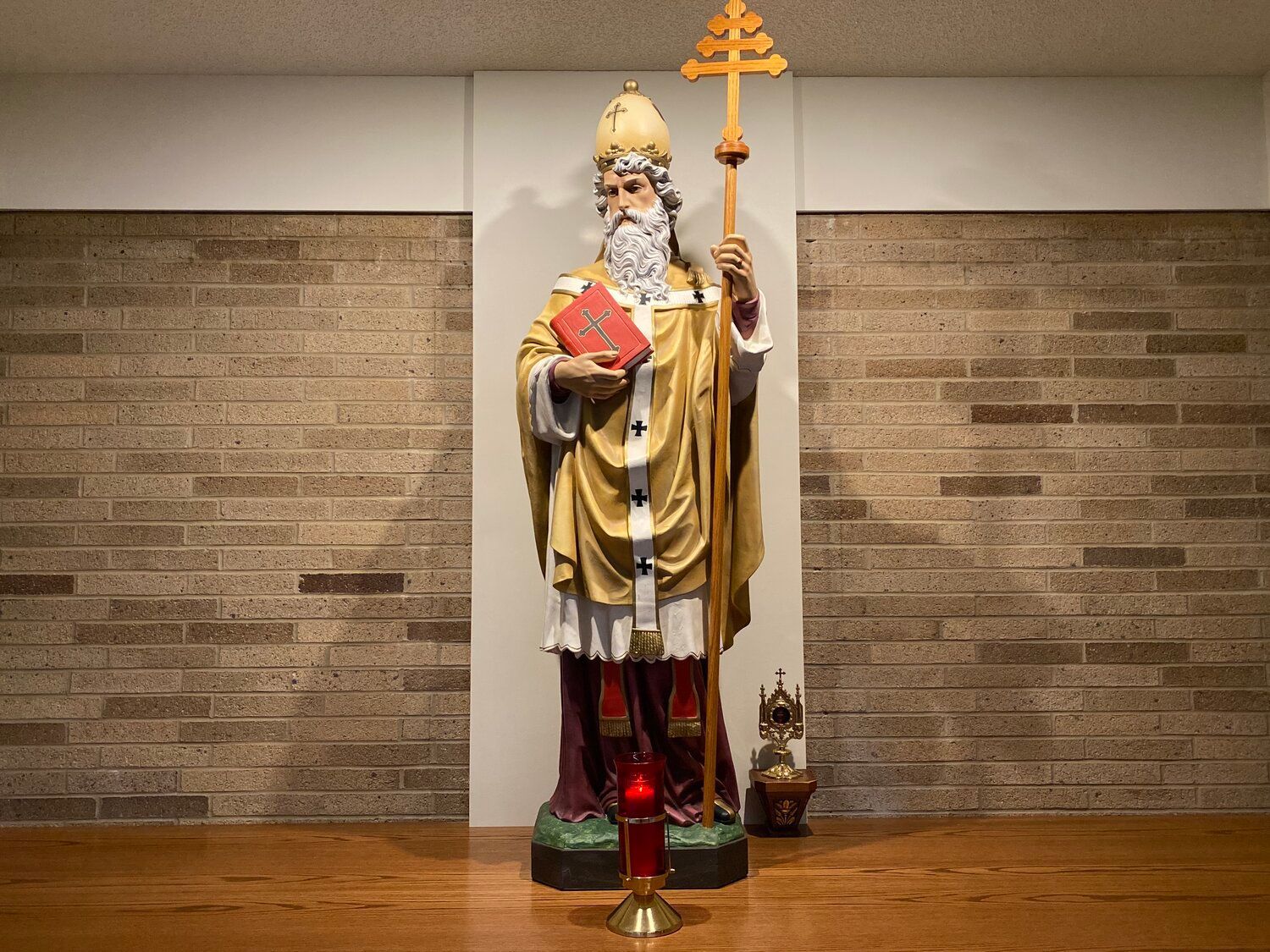 A statue of St. Leo the Great holding a bible and a staff in front of a brick wall.