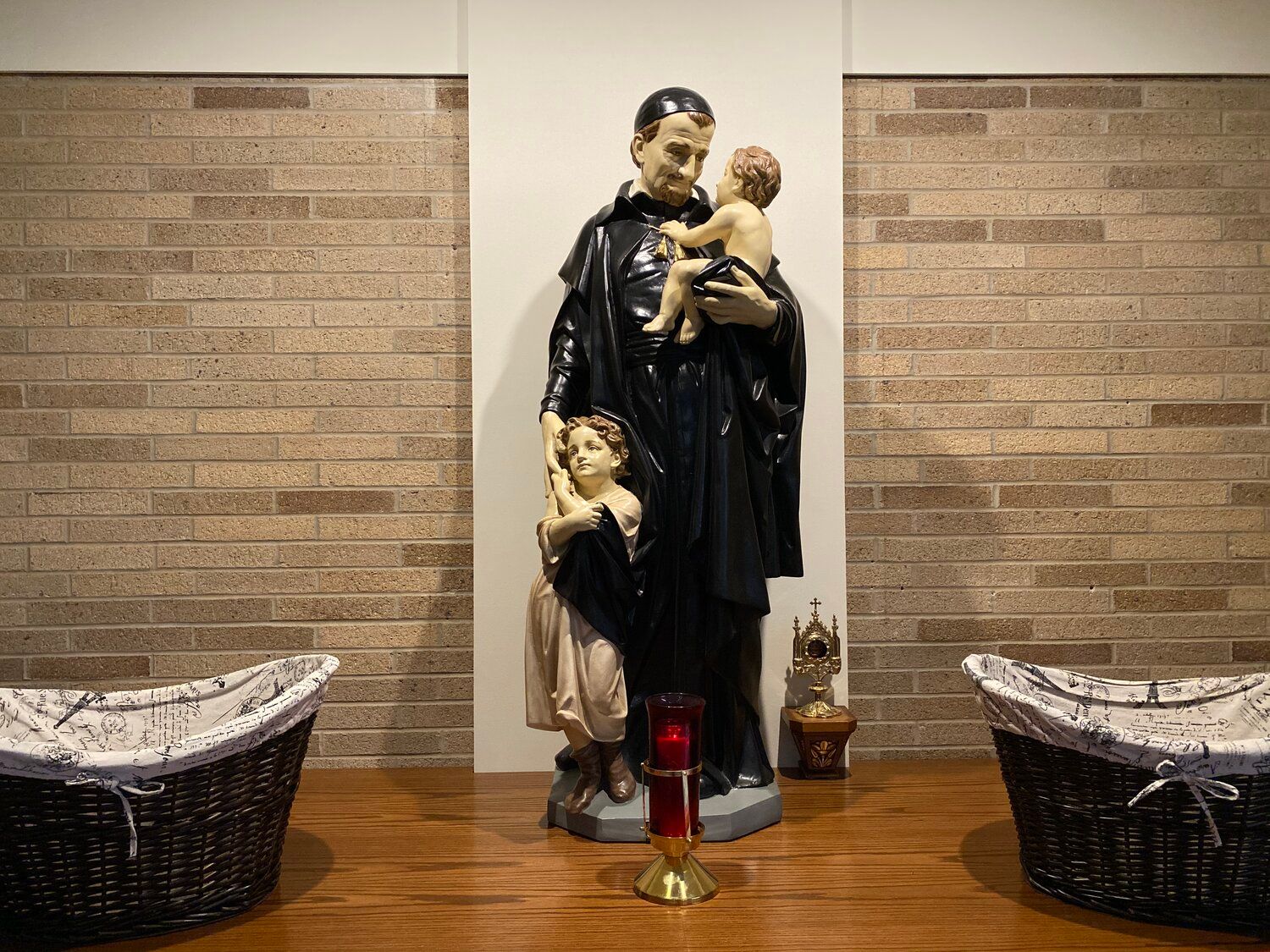 A statue of St. Vincent de Paul holding two children in front of a brick wall