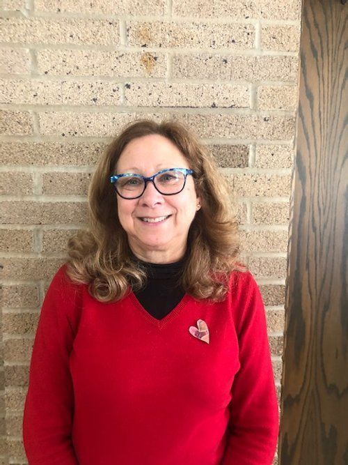 A woman wearing glasses and a red sweater is standing in front of a brick wall.