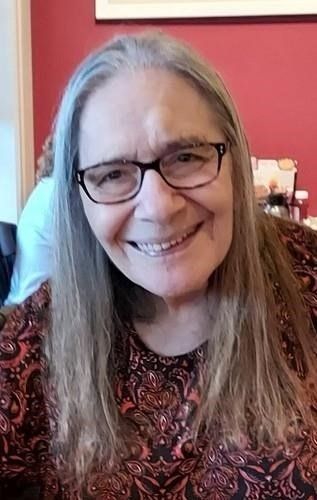 A woman wearing glasses and a paisley shirt is smiling for the camera.