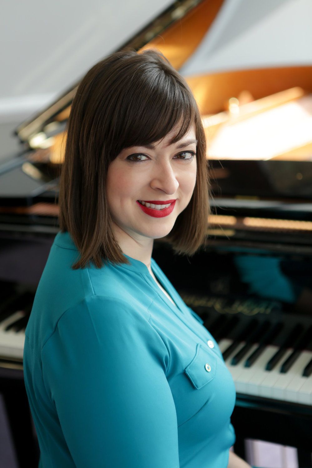 A woman in a blue shirt is sitting in front of a piano.