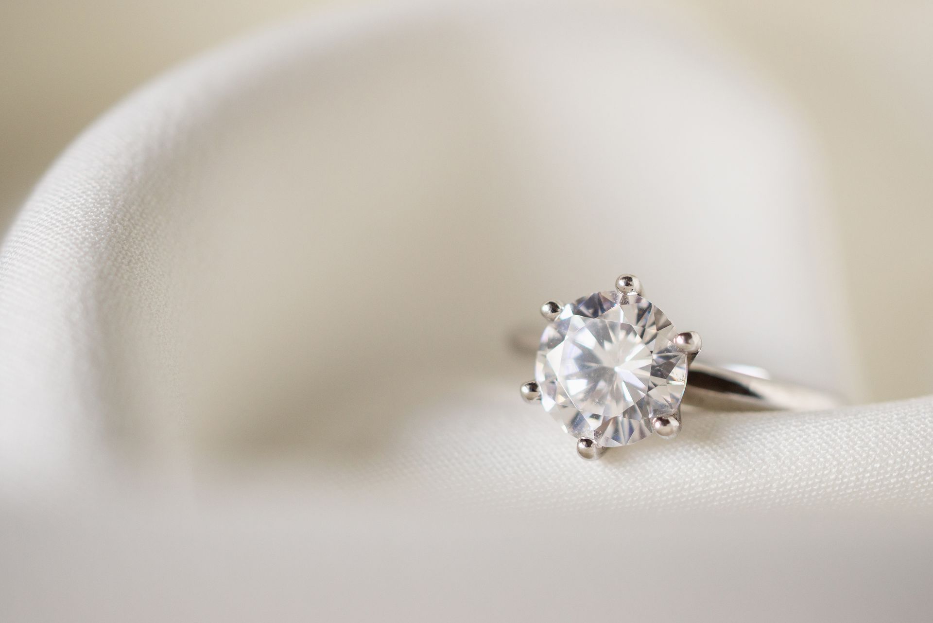 A close up of a diamond ring on a white cloth.