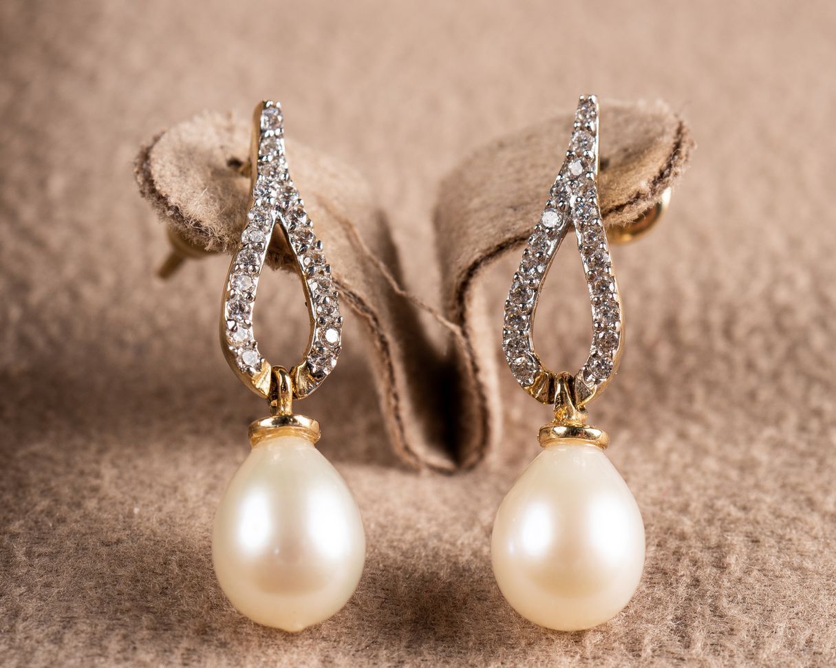 A pair of pearl and diamond earrings are sitting on a cloth.