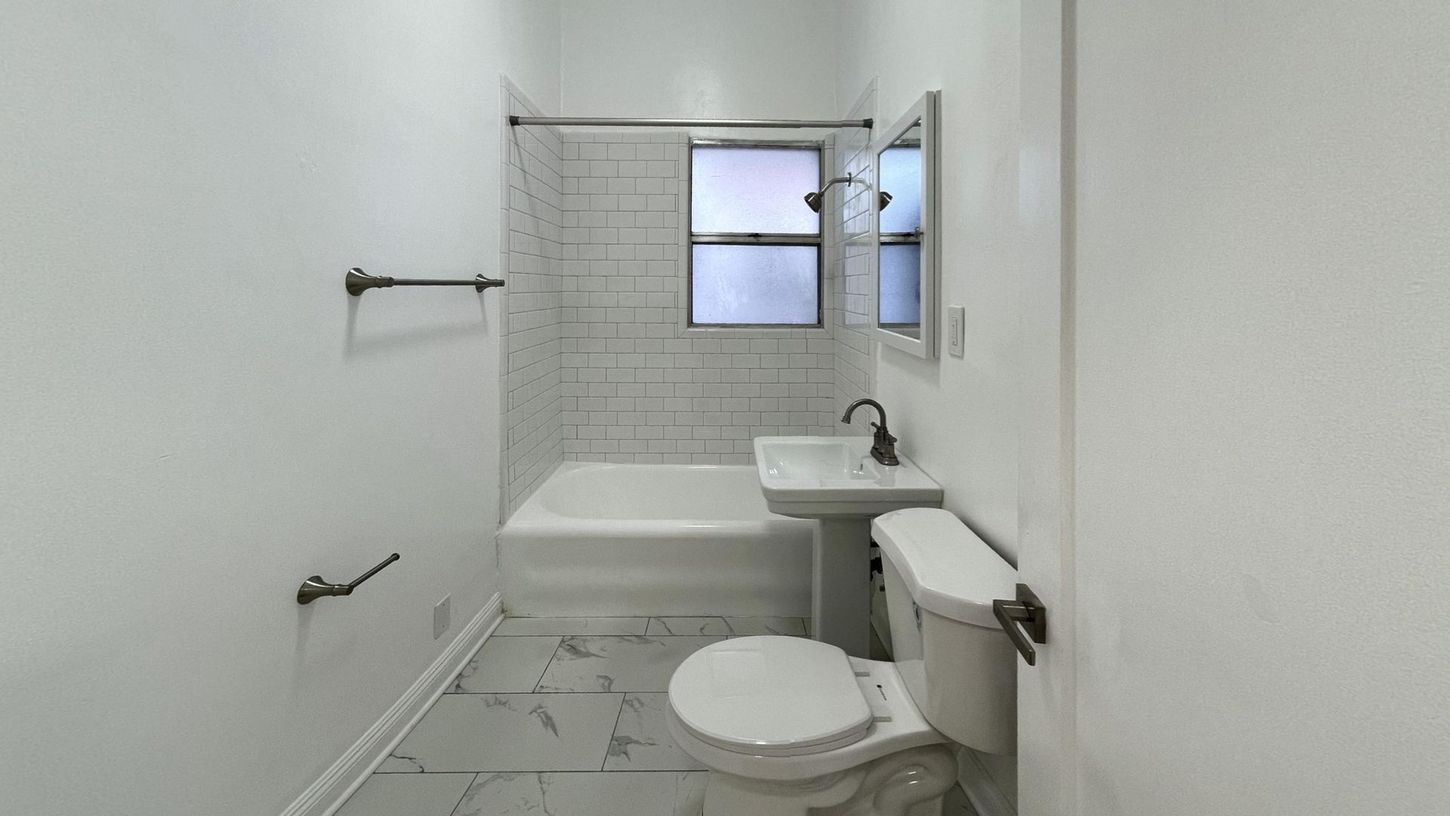 White bathroom with a bathtub, toilet, sink, and window.