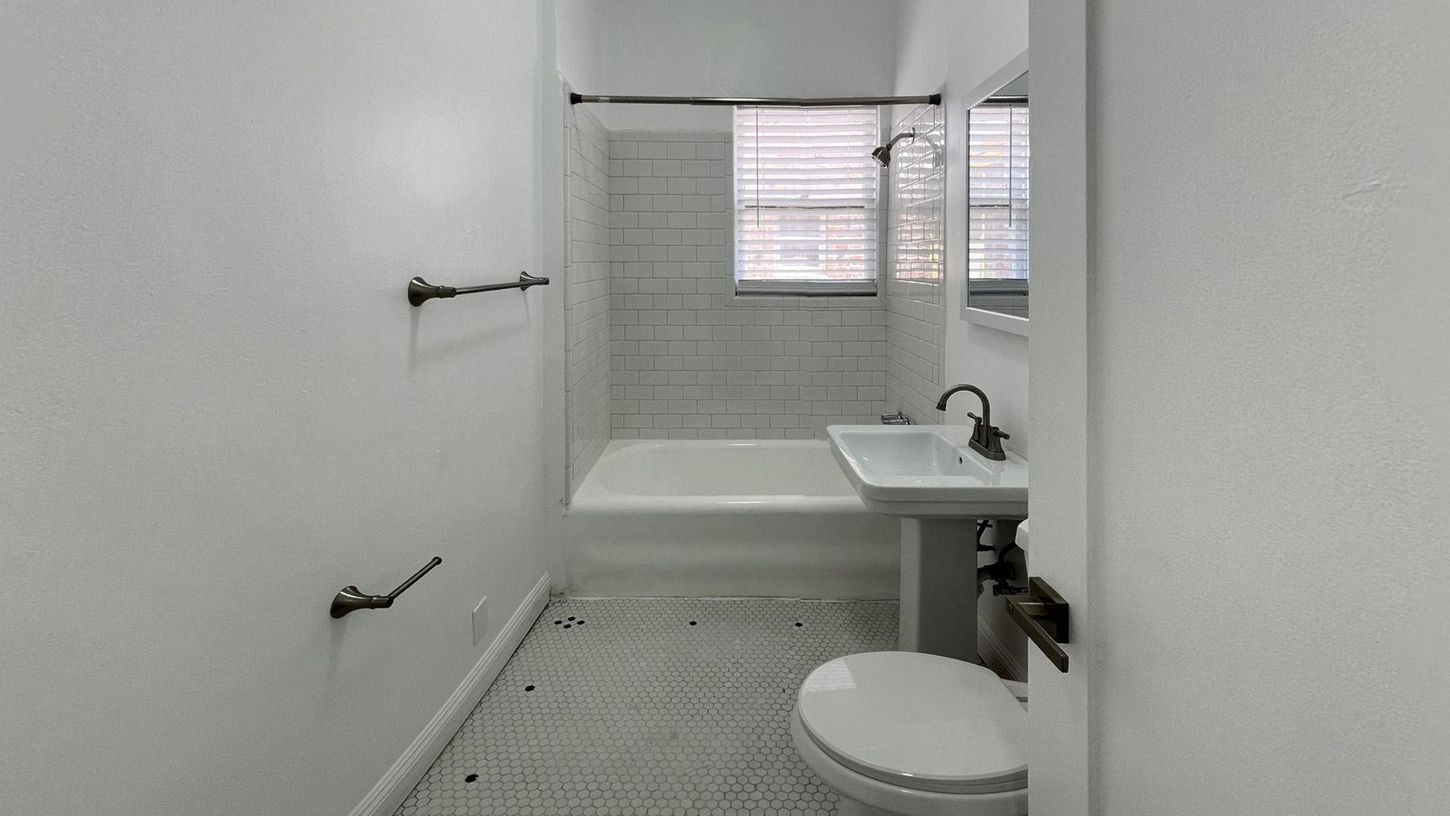 Small, white bathroom with a bathtub, toilet, sink, and window.