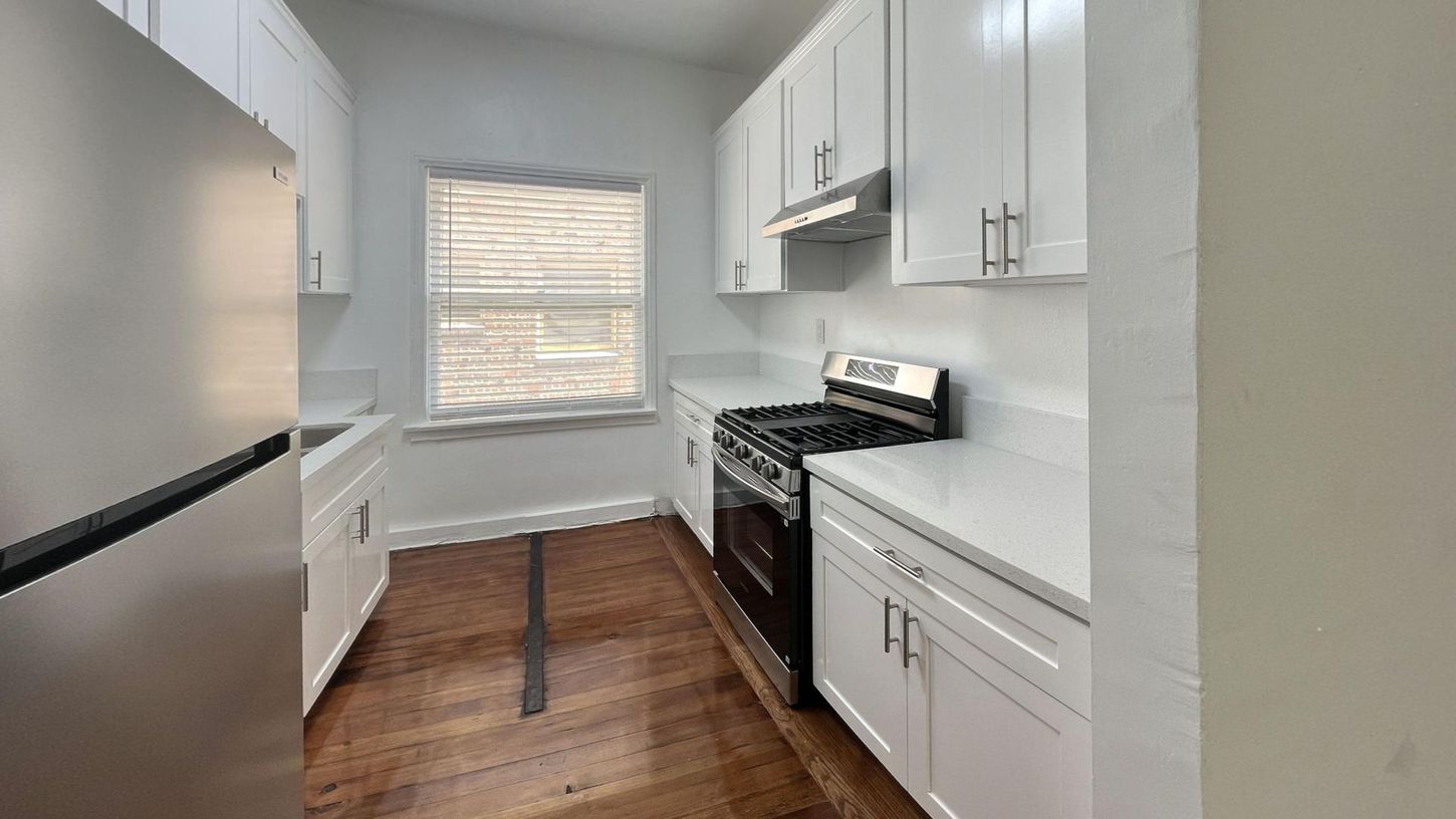 White kitchen with stainless steel appliances, white cabinets, and dark wood floors.