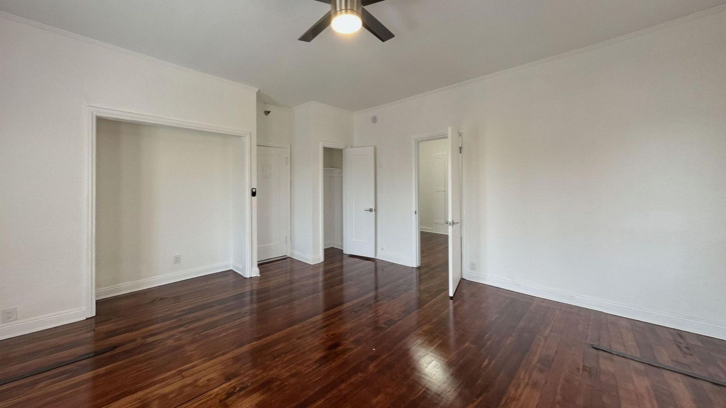 Empty room with hardwood floors, white walls, closet, and two doorways. Ceiling fan.