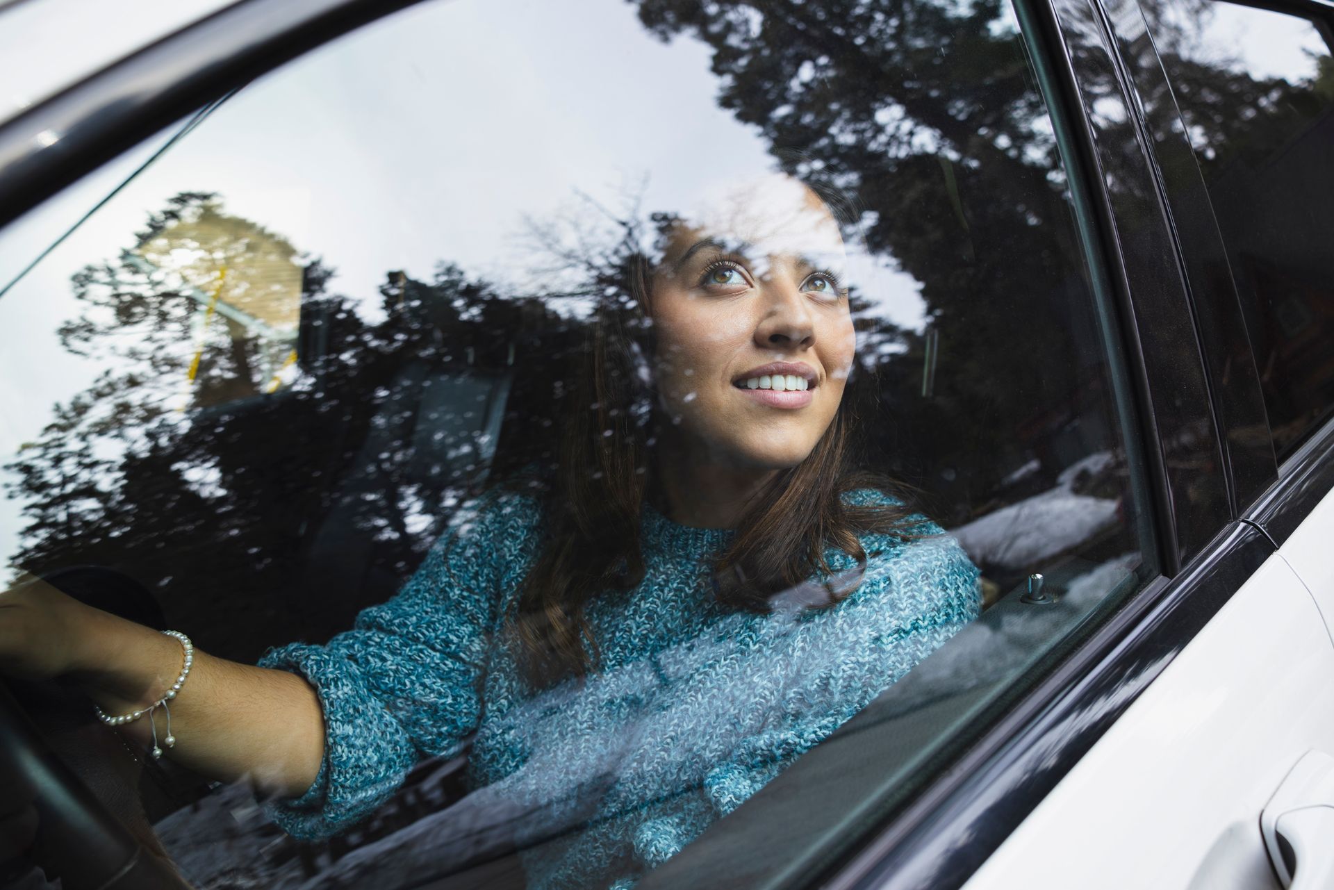 Smiling young woman driving car while looking out through window