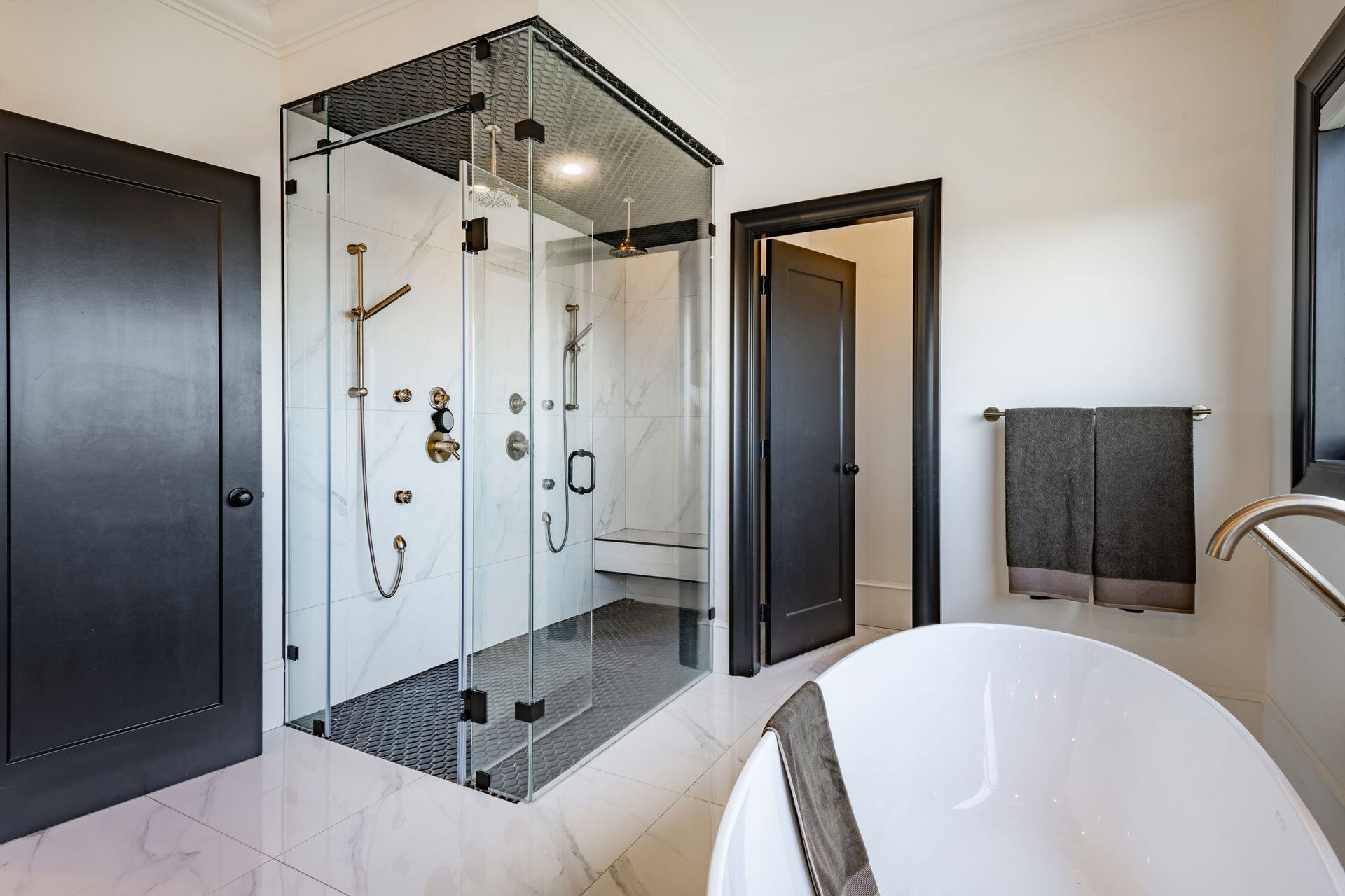 A black and white bathroom with a standalone bathtub and frameless shower doors.