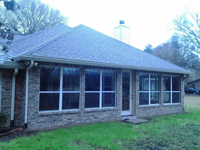 A brick house with a screened in porch and lots of windows.