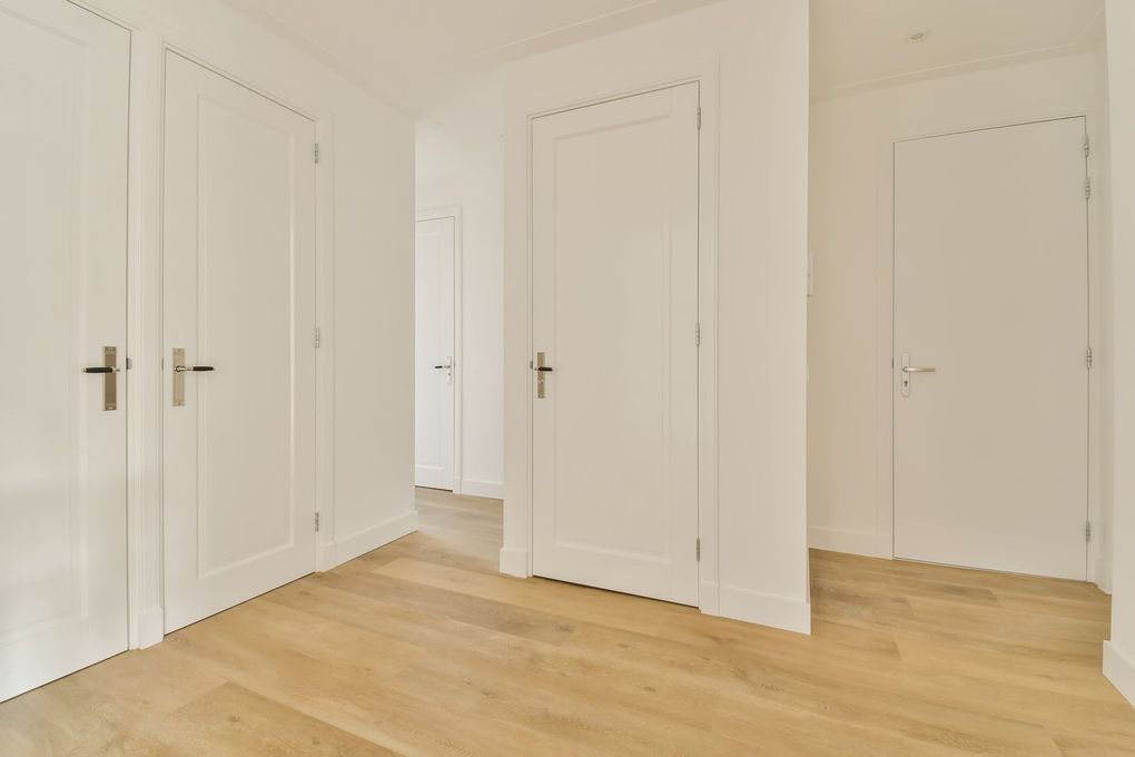 A hallway with white doors and wooden floors in a house.