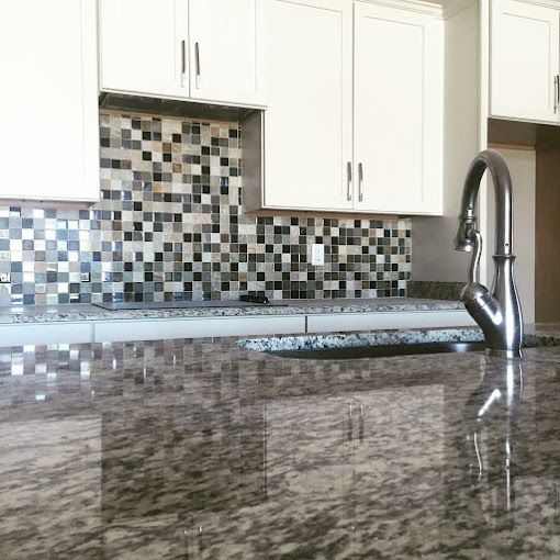 A kitchen with granite counter tops, white cabinets, a sink and a faucet.
