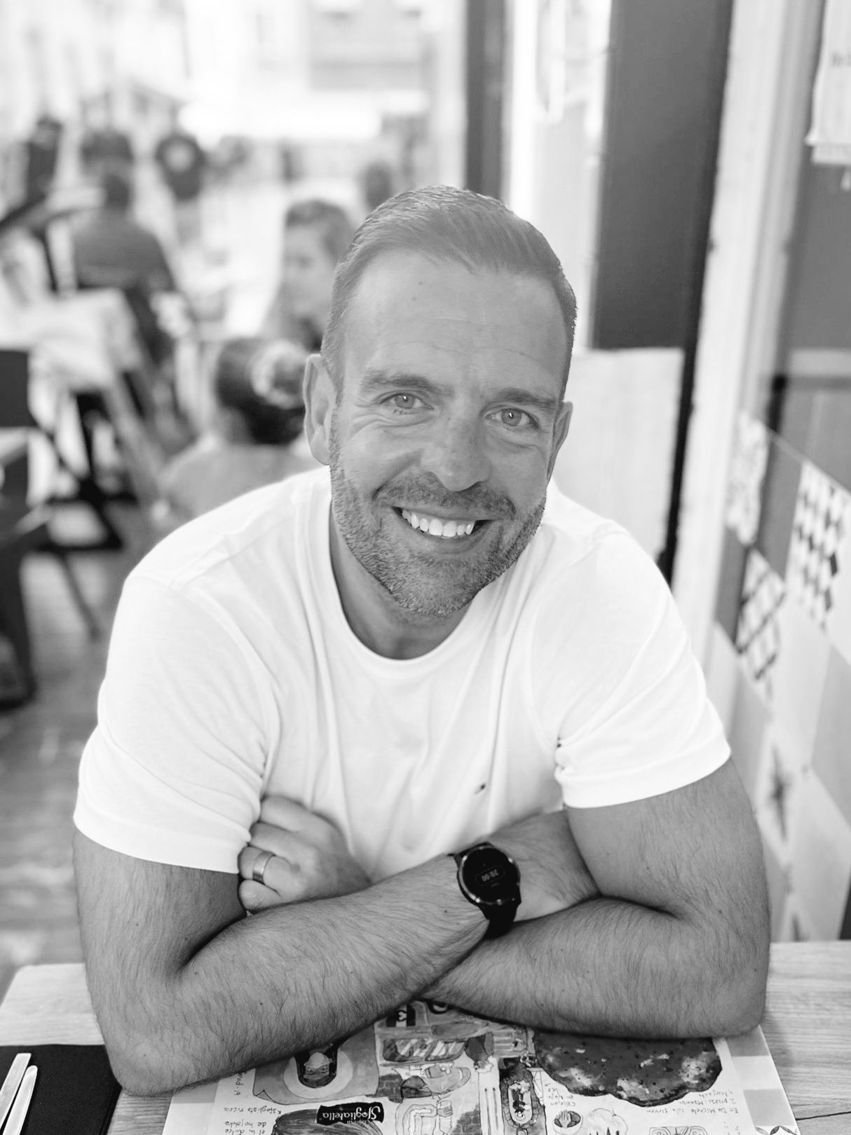 A man with a beard is sitting at a table with his arms crossed and smiling.