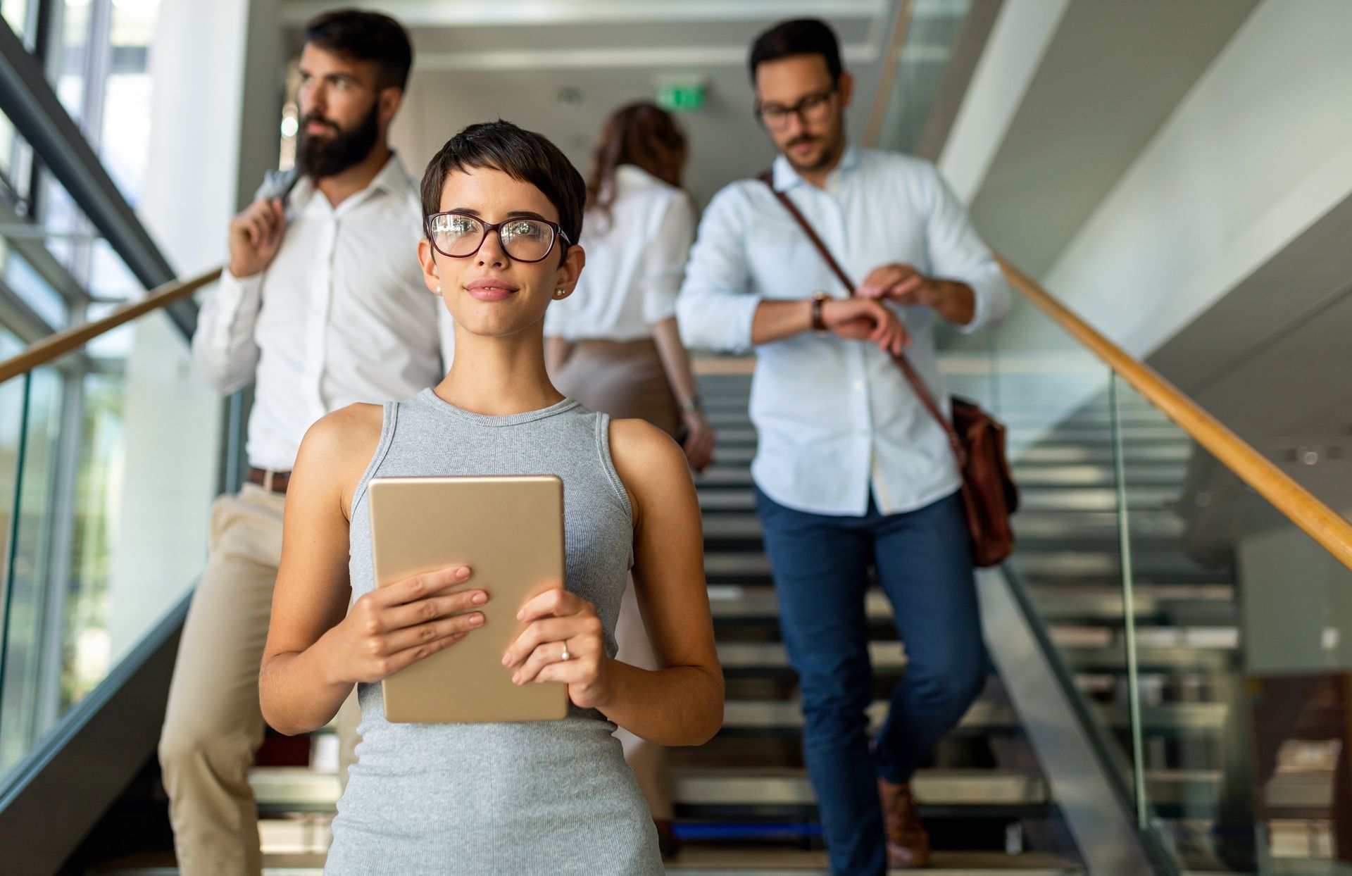 A woman is holding a tablet while walking down stairs.