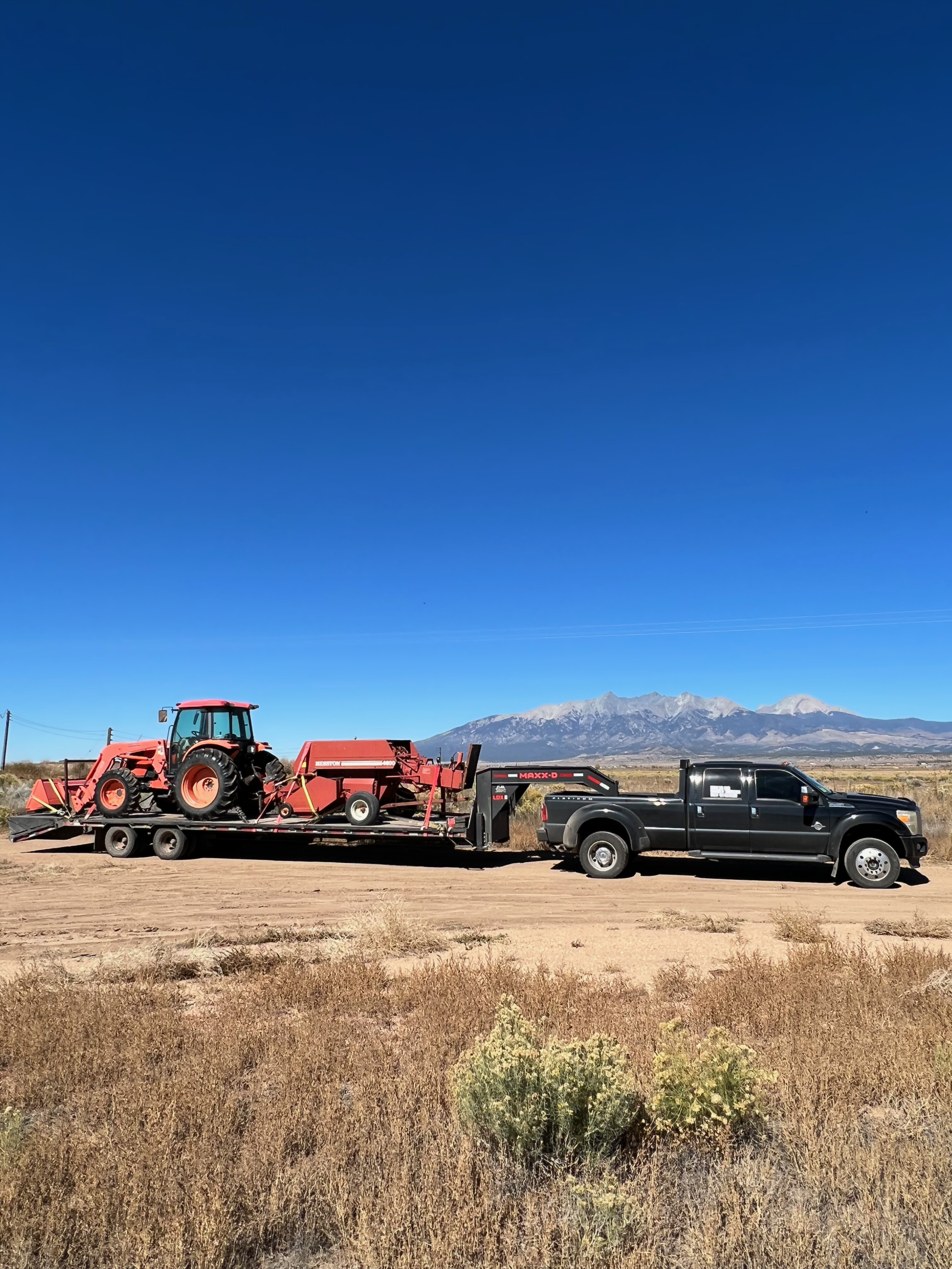 orange construction equipment on flatbed gooseneck trailer being hauled by haul3d across colorado mountains