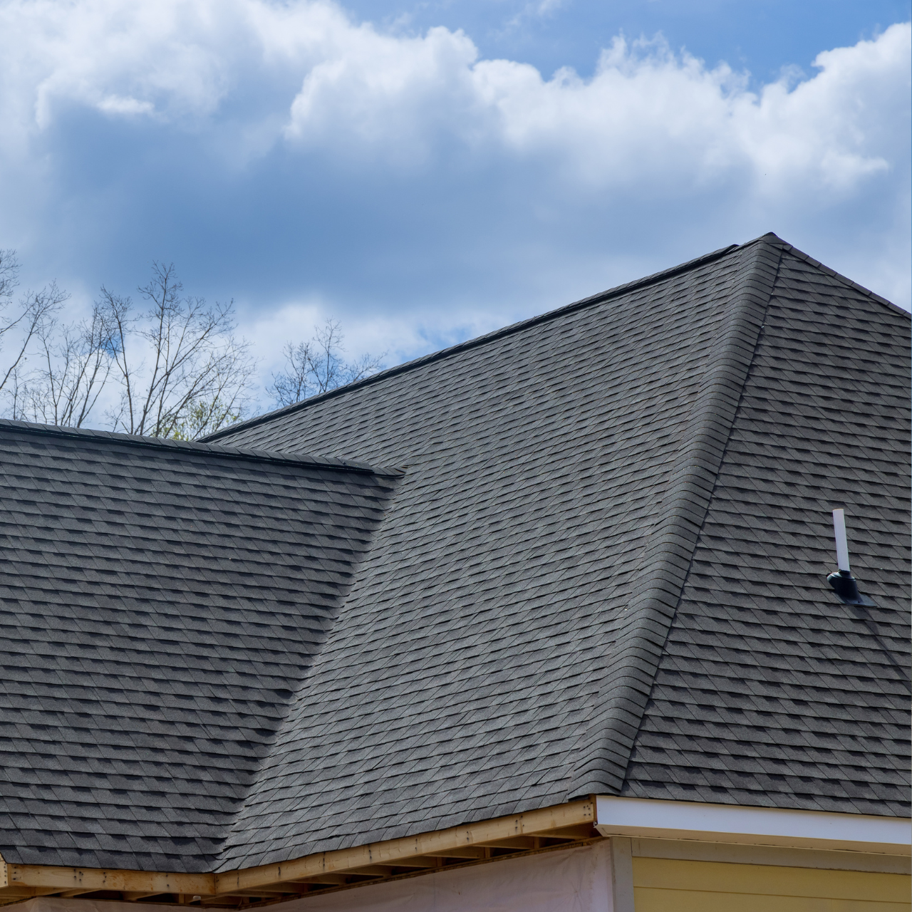 A gray shingled roof under a blue, cloudy sky, with unfinished wooden eaves visible on the lower edge.