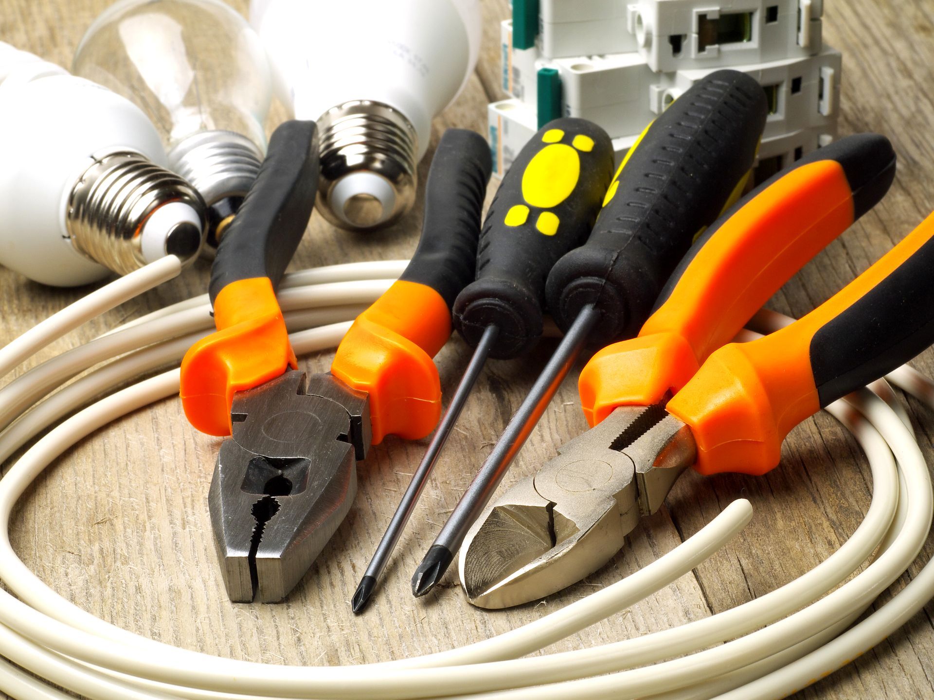 Electrical tools and light bulbs on a wooden surface: pliers, screwdrivers, wire, and bulbs.