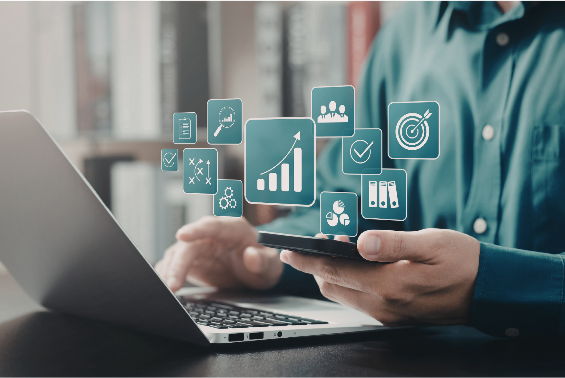 Person using a smartphone beside a laptop with floating business analytics icons
