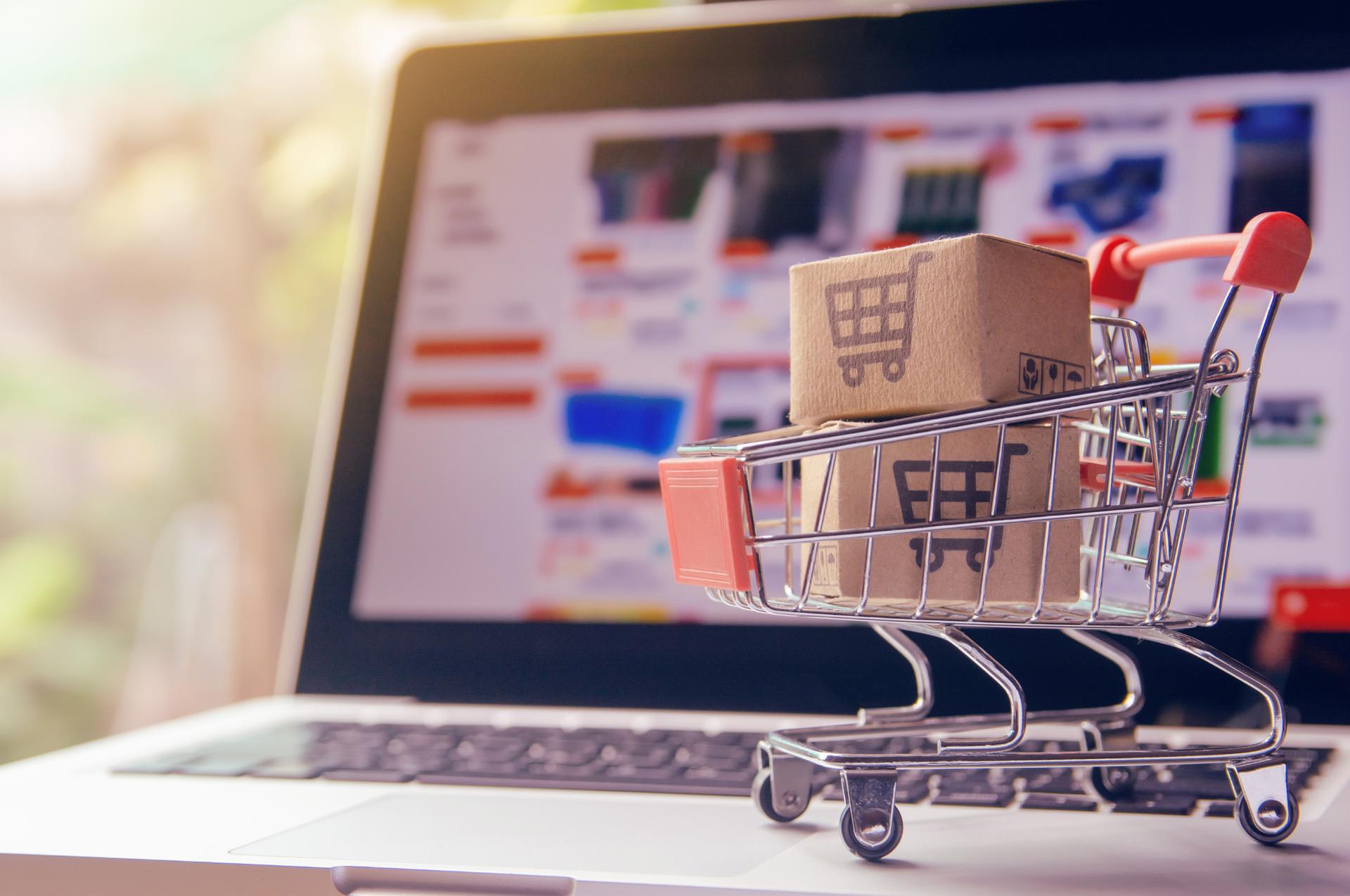 Shopping cart with cardboard boxes in front of a laptop screen, suggesting online shopping