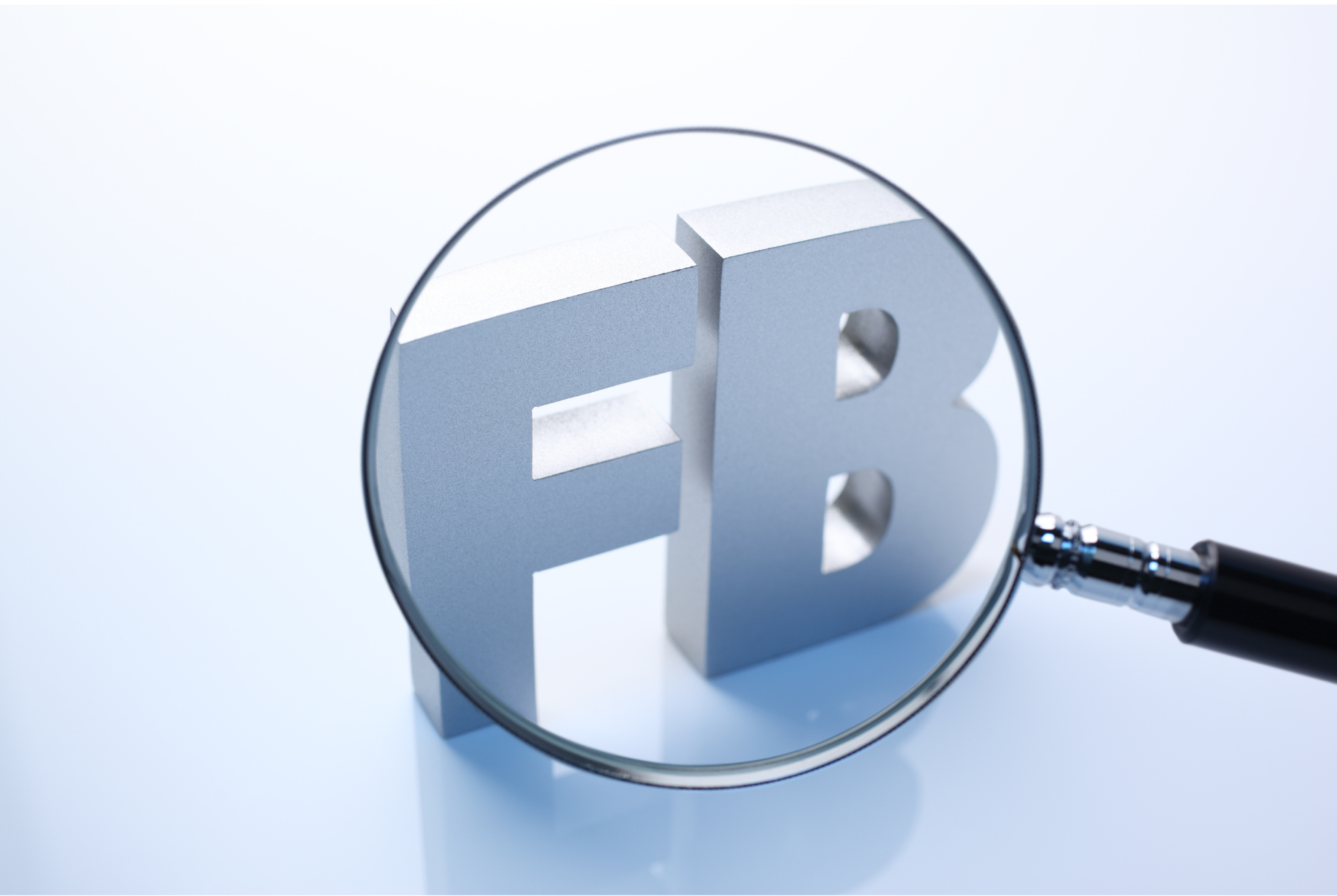 Magnifying glass over metallic Facebook logo on a white background