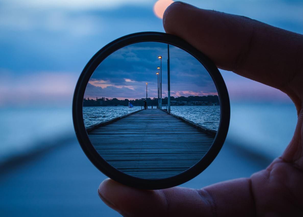 A person is holding a lens with a view of a pier in it.