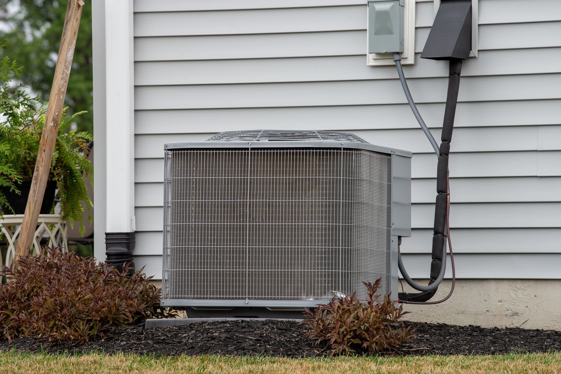 Two outdoor air conditioning units on gravel next to a wooden wall.