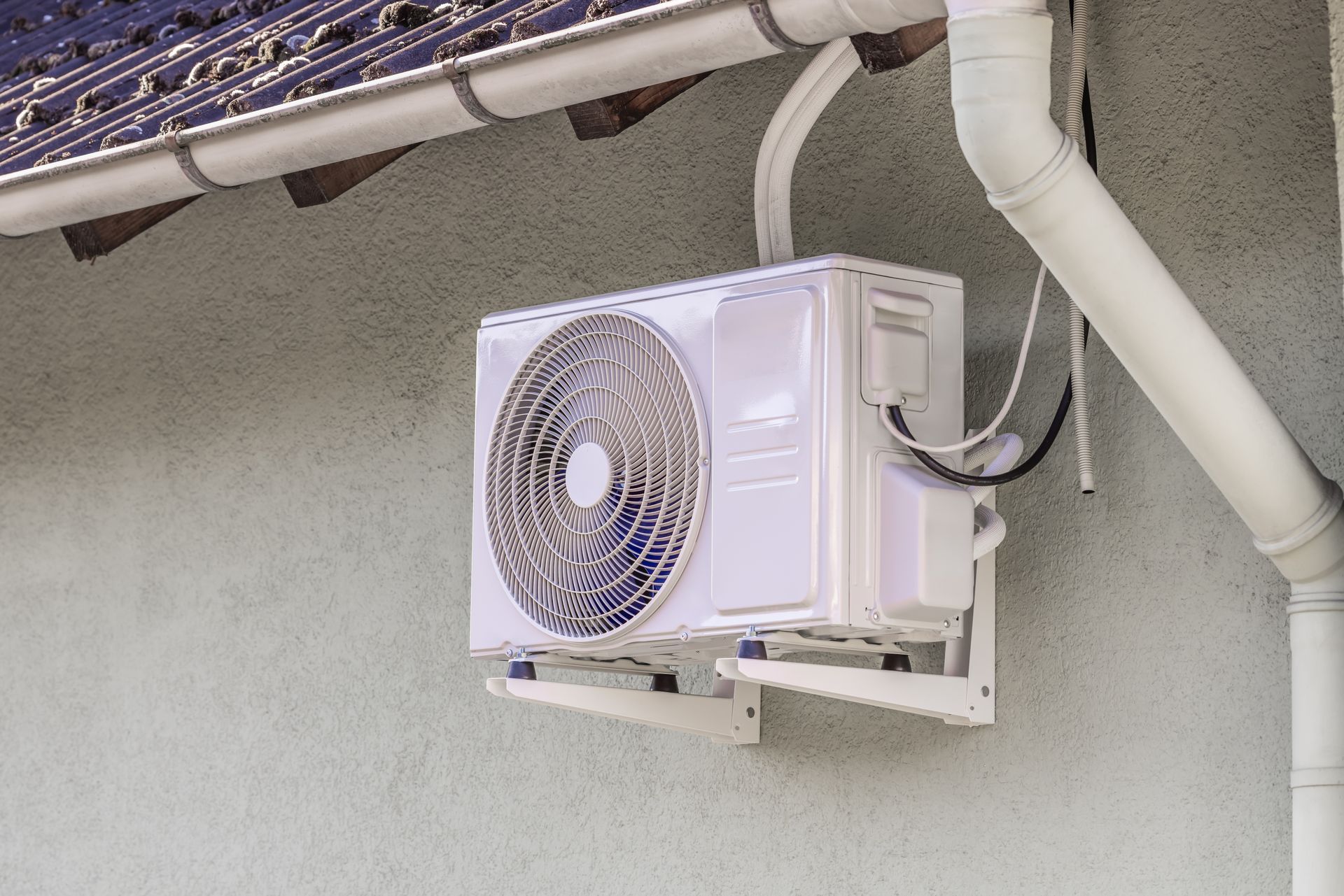 Two outdoor air conditioning units on gravel next to a wooden wall.