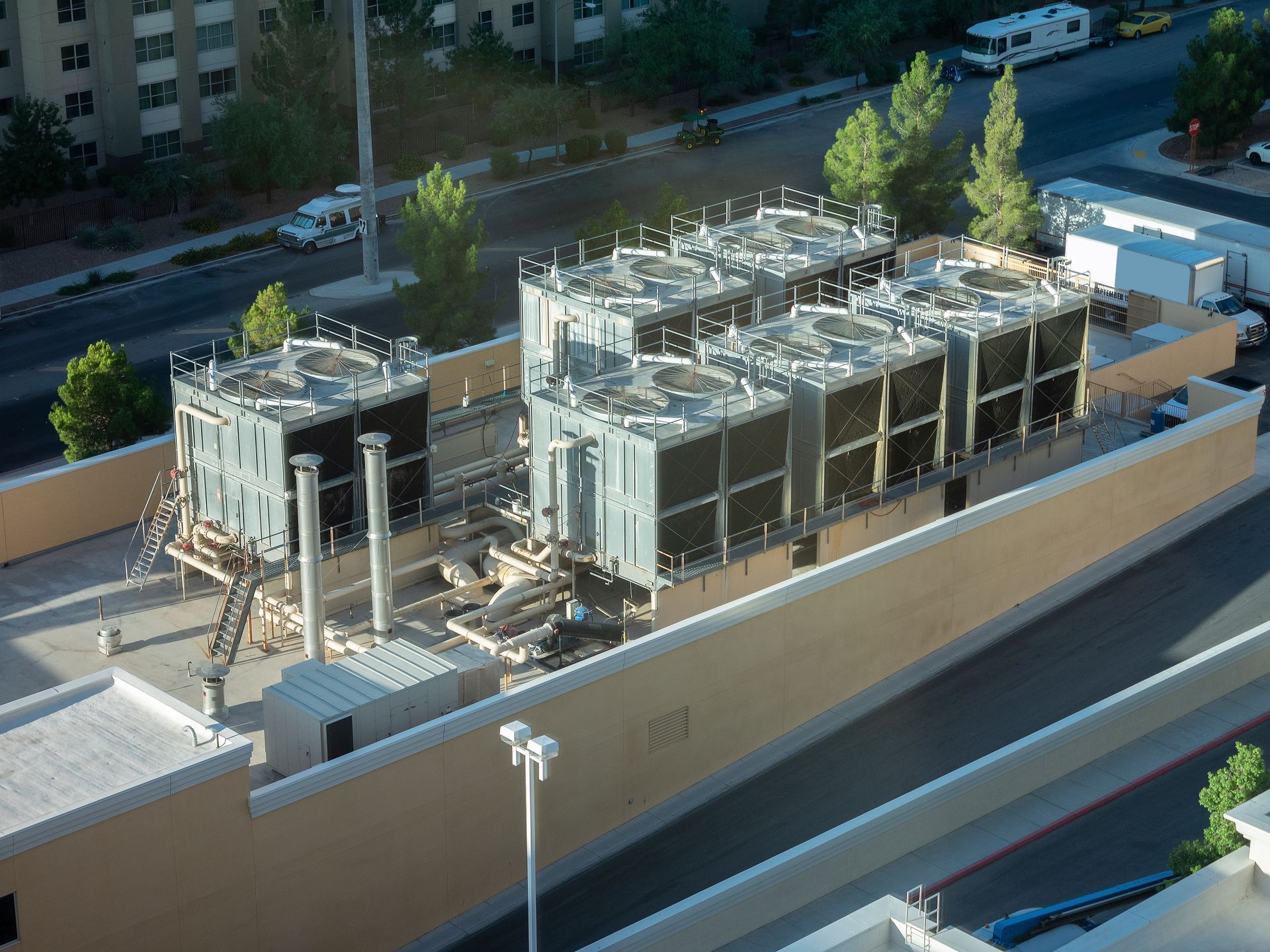 Large industrial rooftop cooling units on a tan building. Trees and street in background.