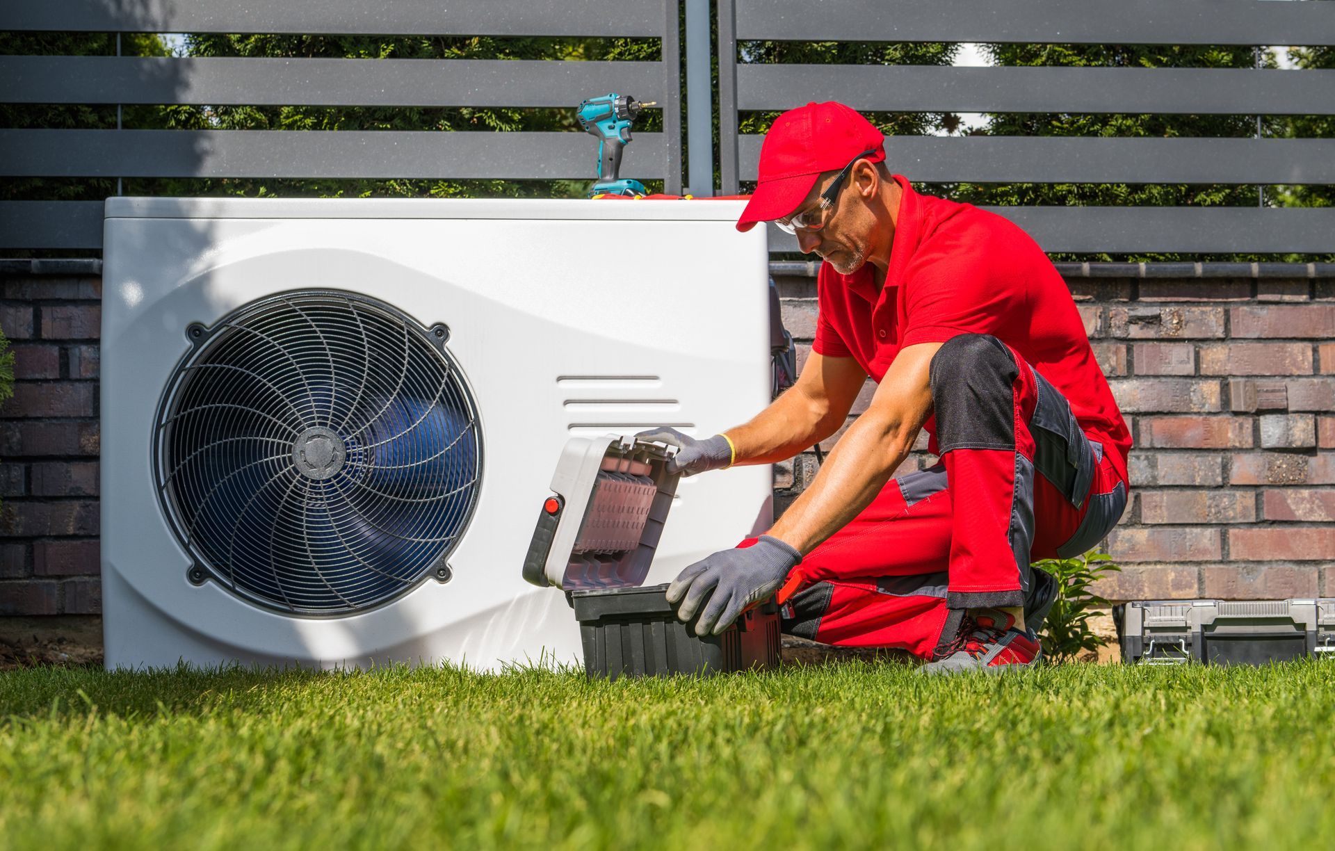 Technician in red uniform inspecting heat pump, in a yard.