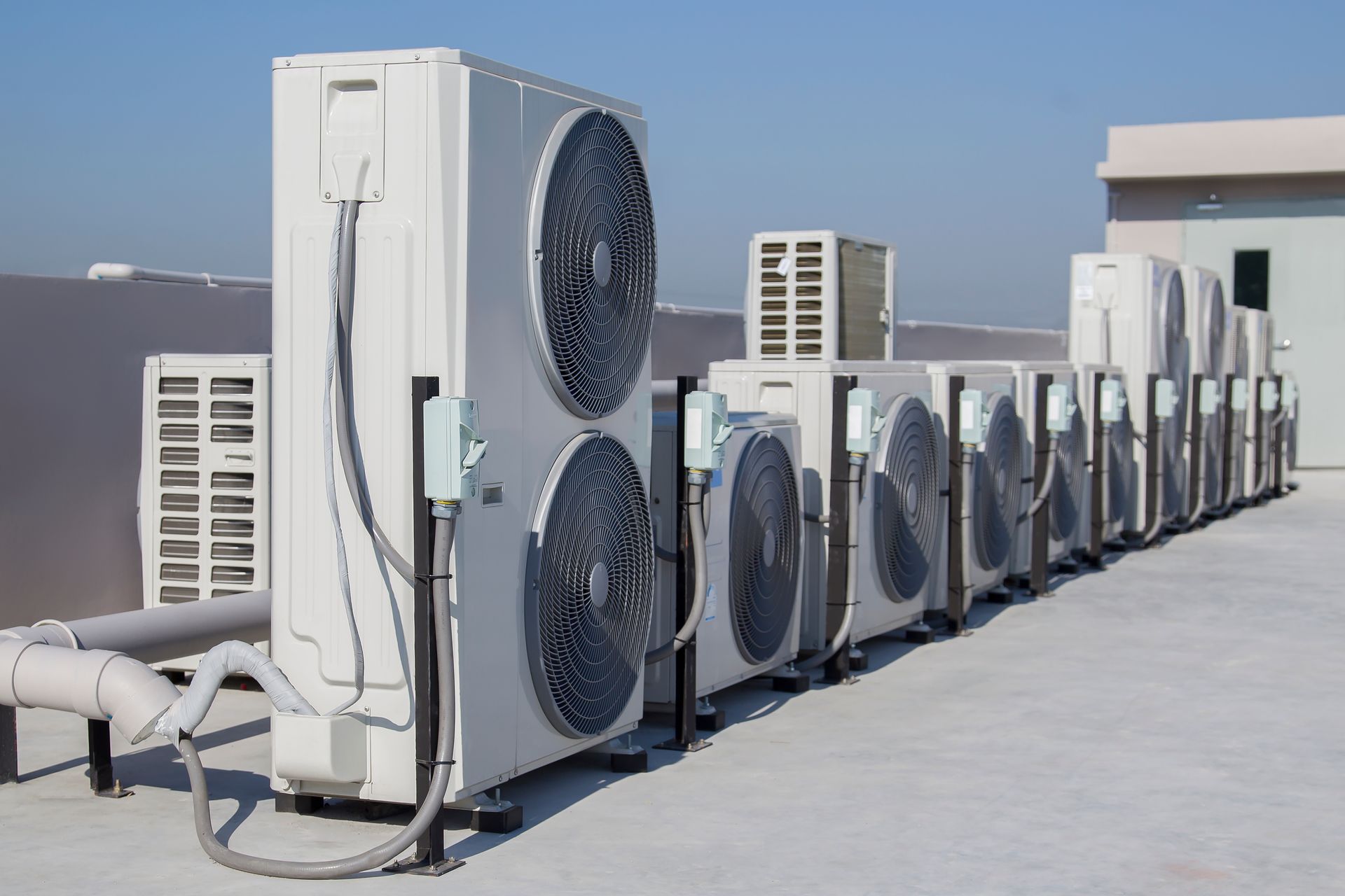 Air conditioning units lined up on a rooftop. White metal, fans visible.