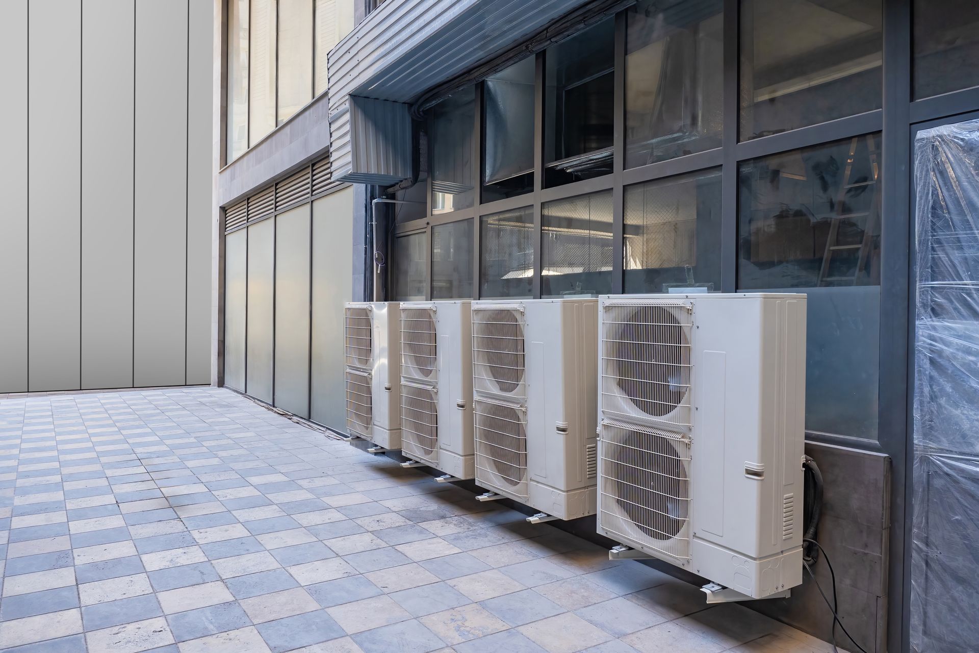 Row of white air conditioning units mounted on a building's exterior wall.