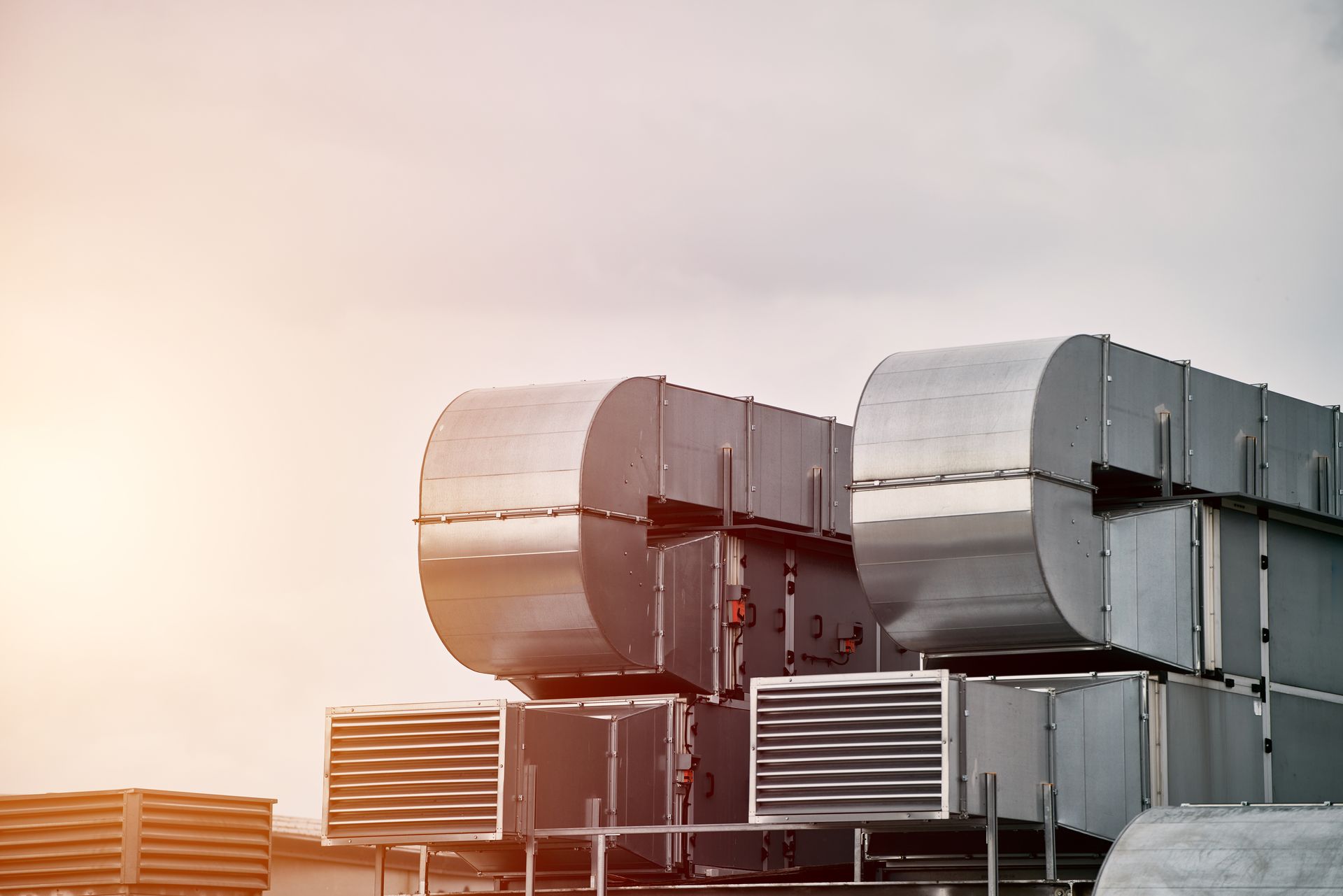 HVAC units on a rooftop against a cloudy sky, with sunlight.