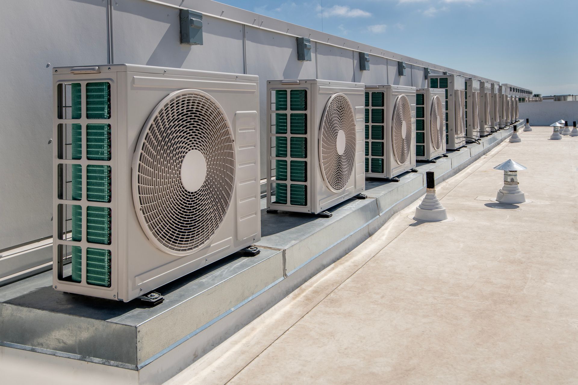 Row of white air conditioning units on a rooftop, sunny day.