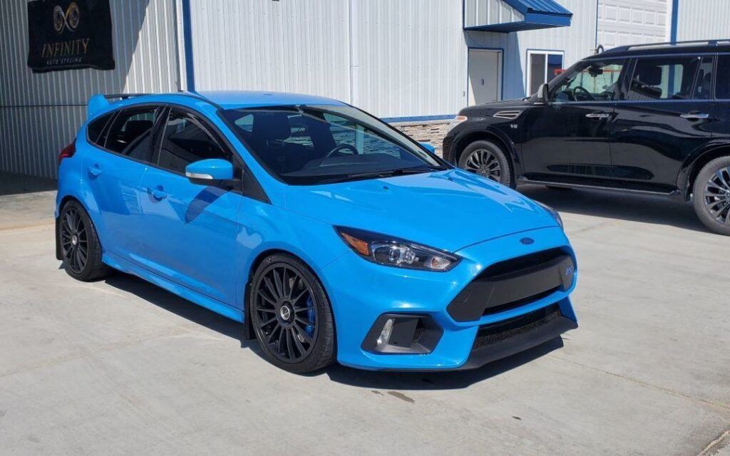 A blue ford focus rs is parked in a parking lot next to a black suv.