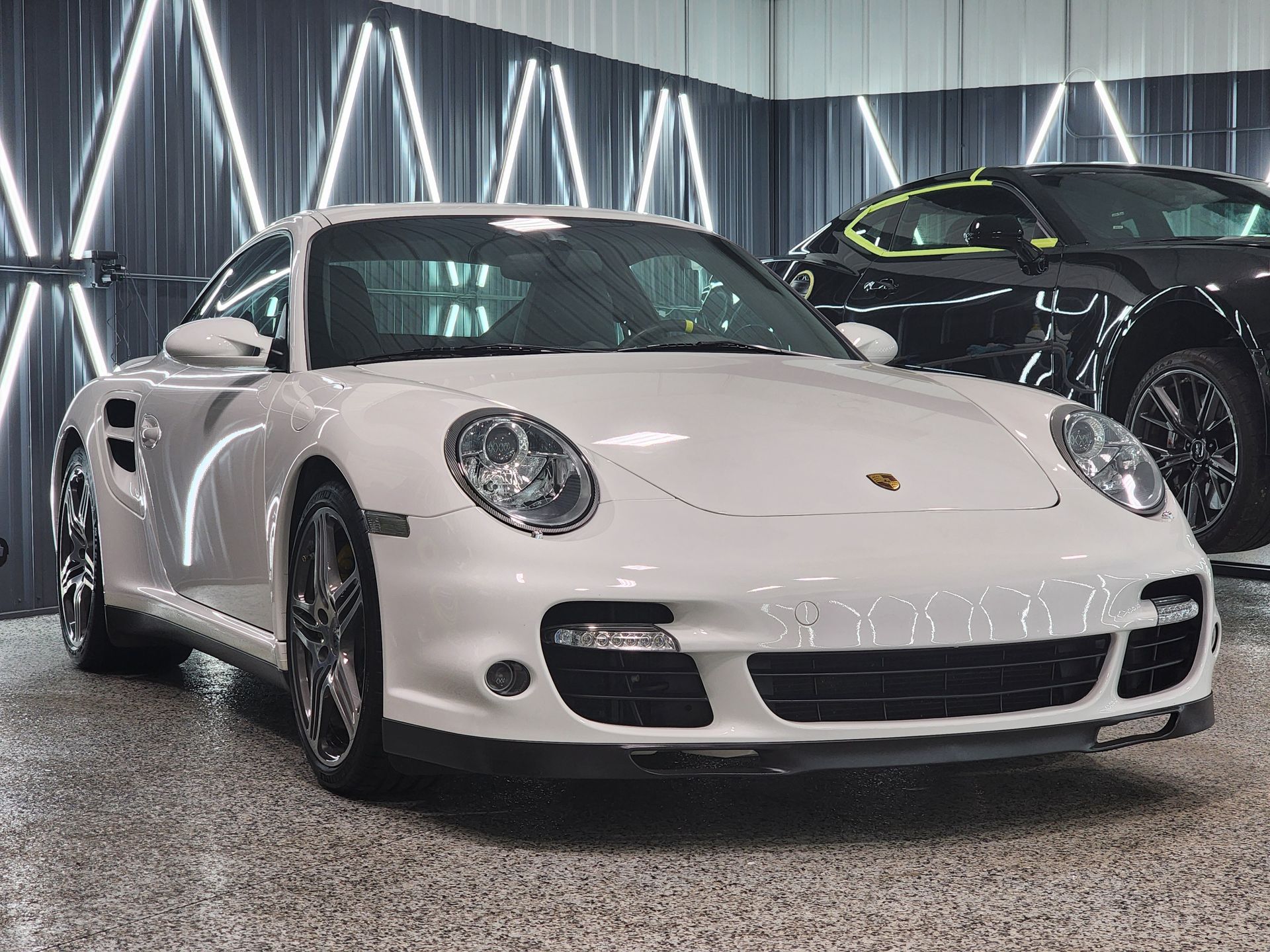 White Porsche sports car in a showroom with a black car in the background.