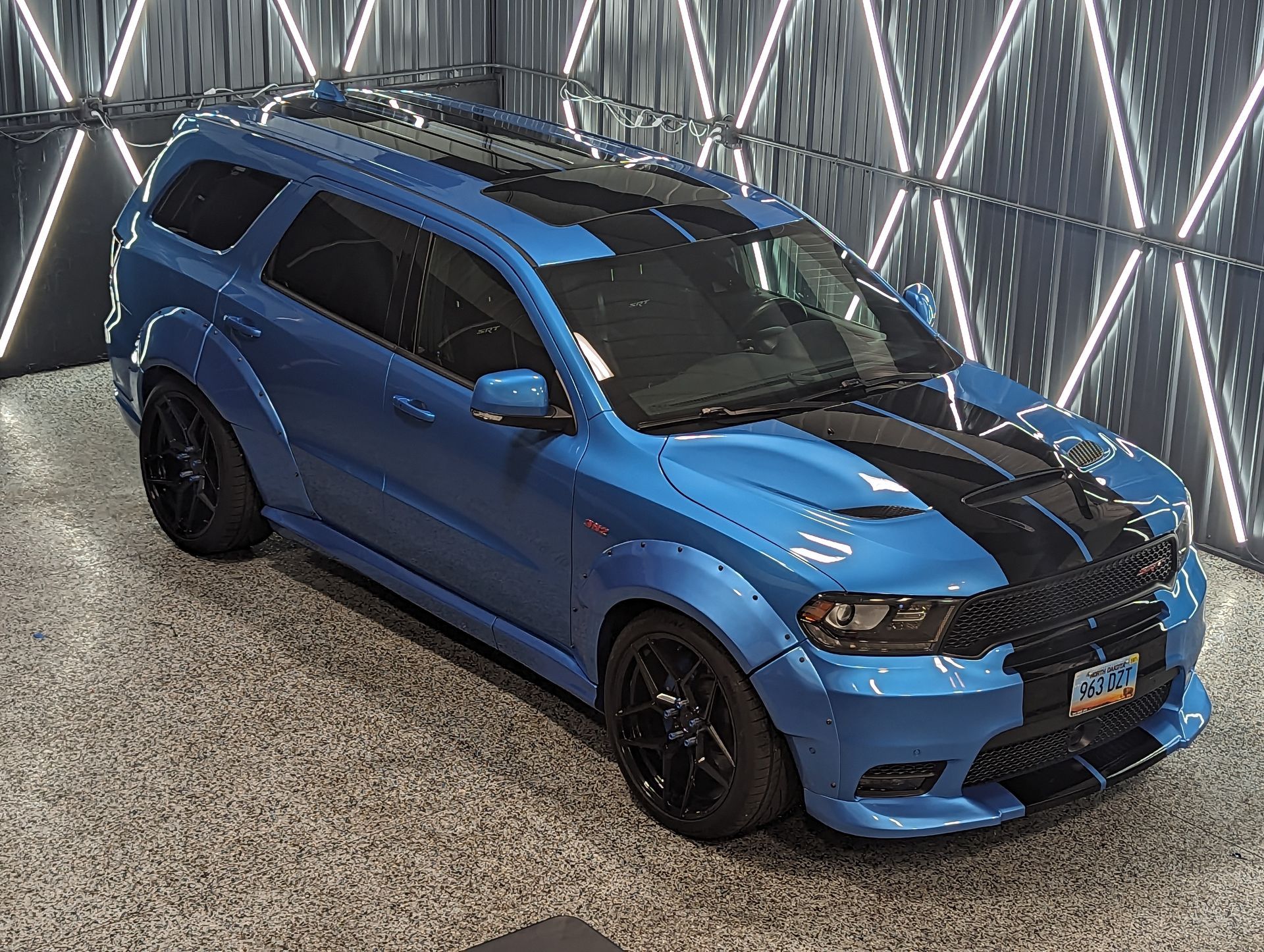 A blue dodge challenger is parked in front of a garage door.
