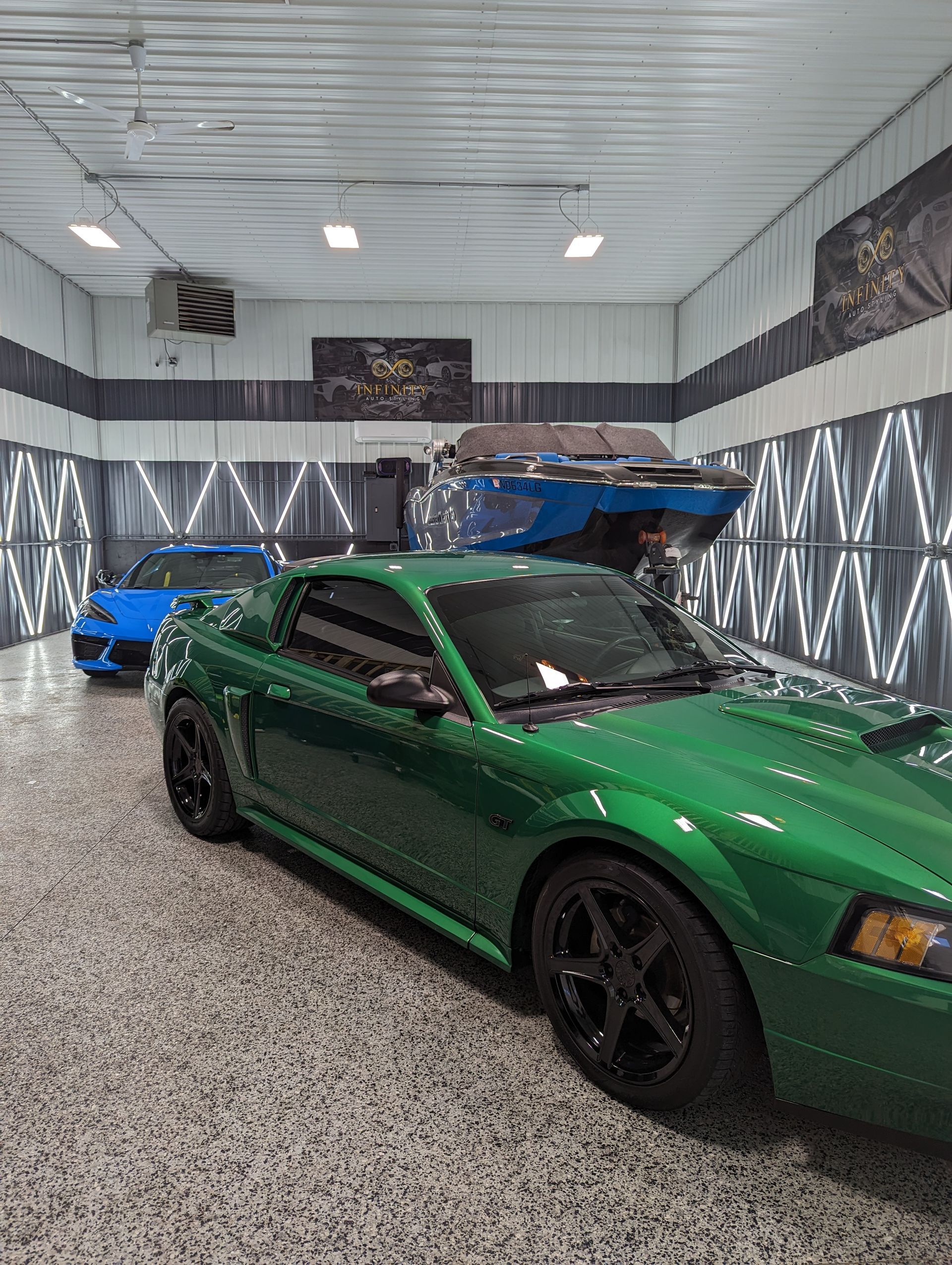 A green mustang is parked in a garage next to a blue lamborghini.