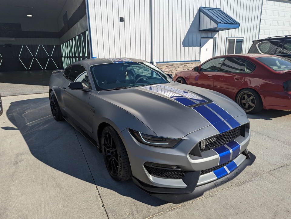 A gray mustang with blue stripes is parked in front of a building.