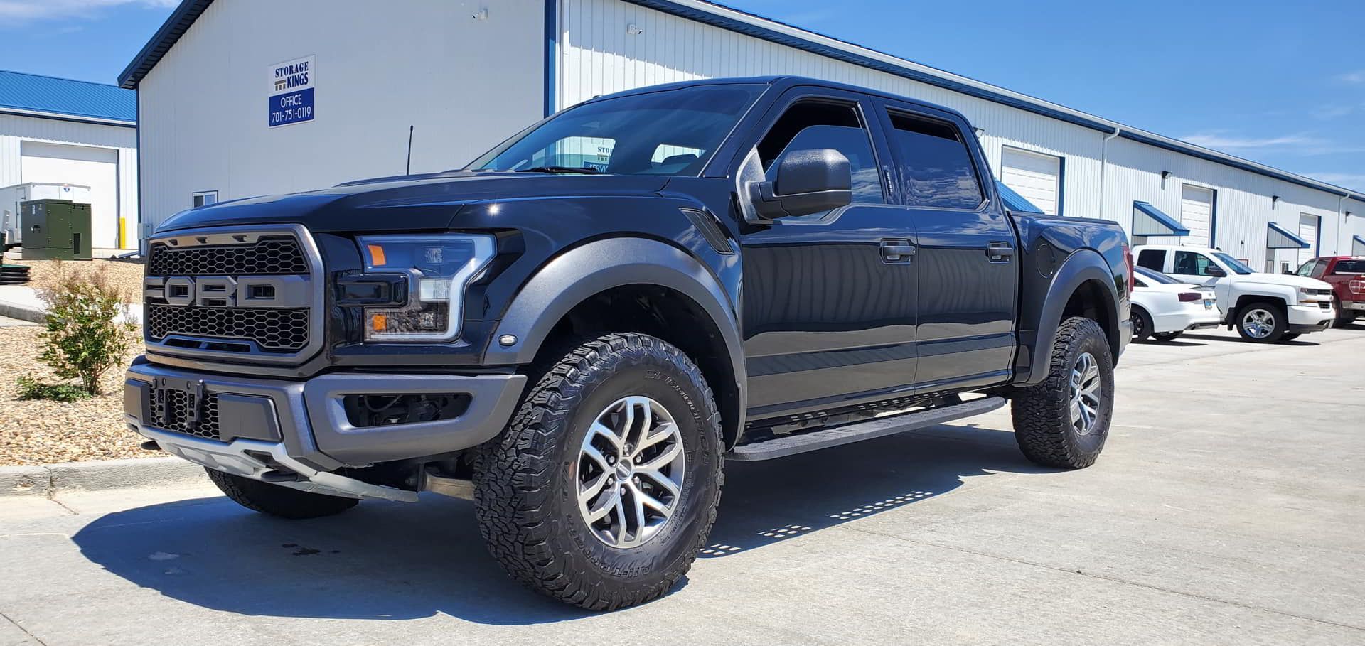 A black ford raptor truck is parked in front of a building.