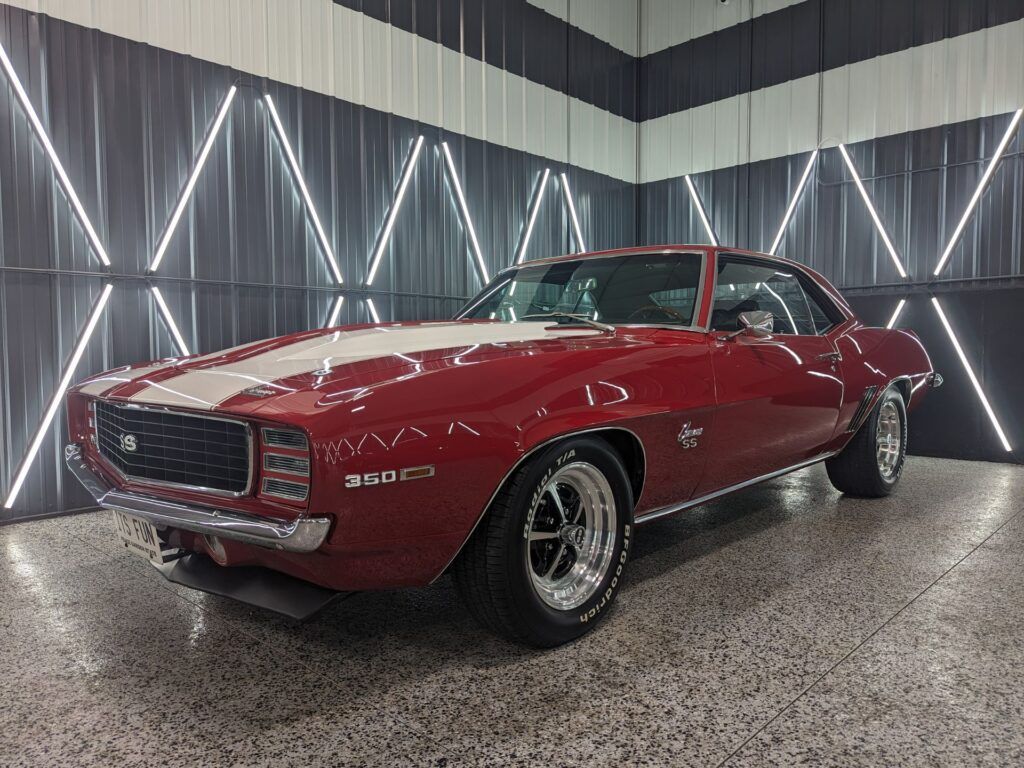 A red and white chevrolet camaro is parked in a garage.