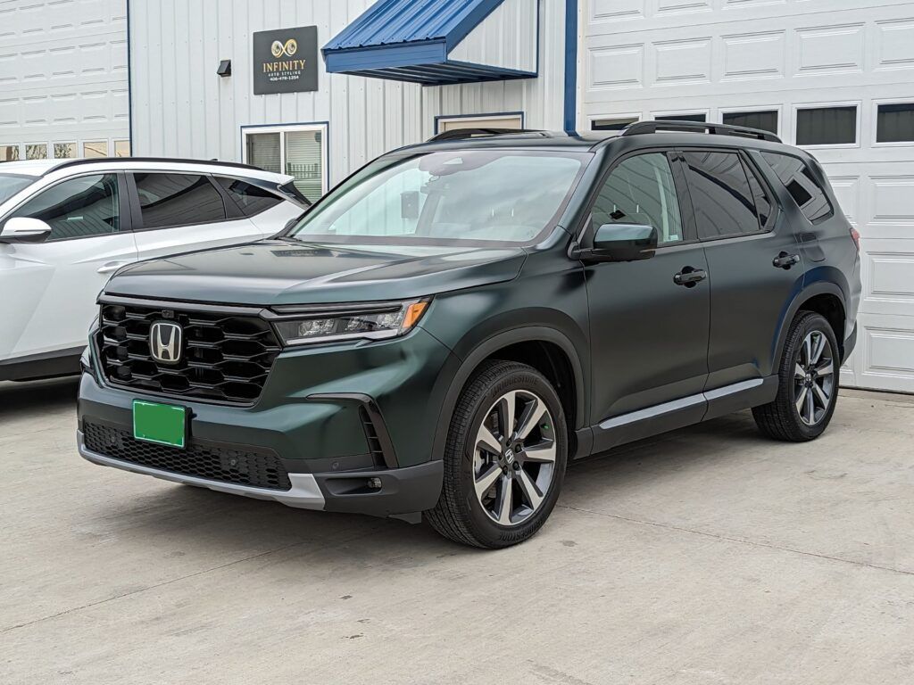 A black honda pilot is parked in front of a garage.