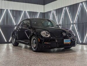 A black volkswagen beetle is parked in a garage.