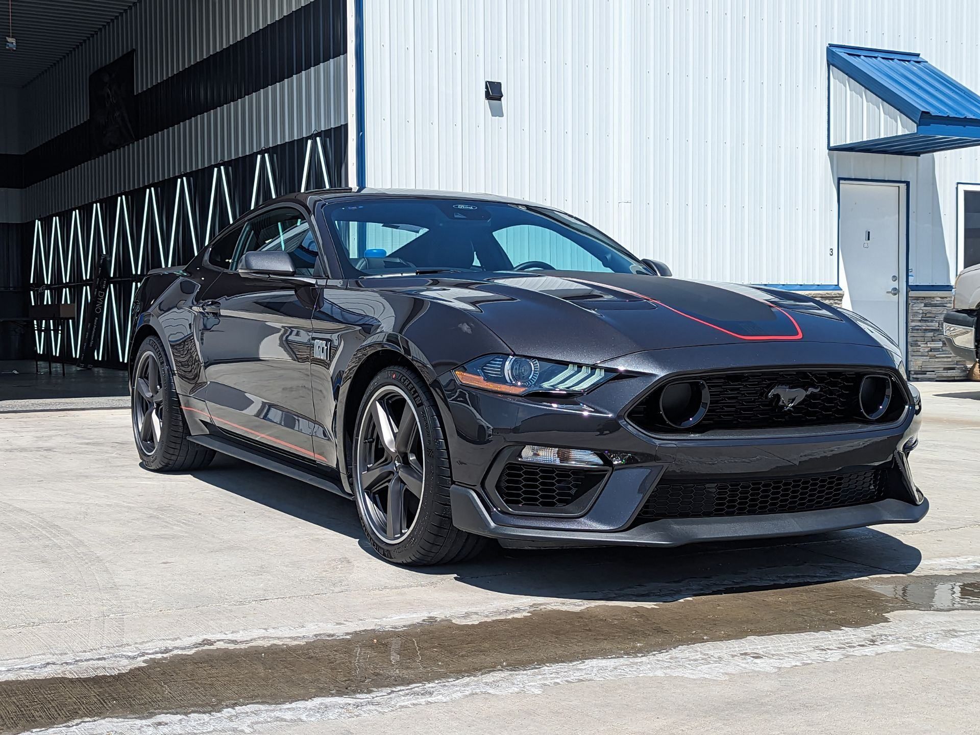 A black ford mustang mach 1 is parked in front of a building.