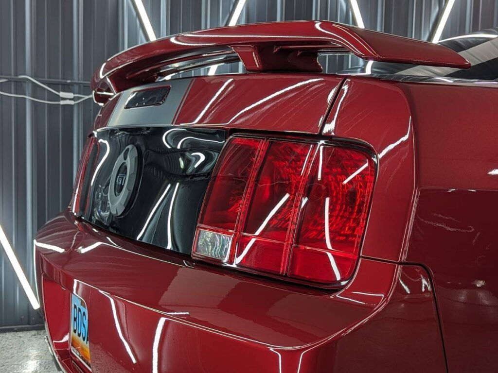 A red mustang with a spoiler on the back is parked in a garage.