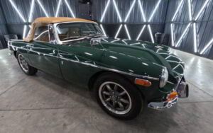 A green sports car with a tan top is parked in a garage.