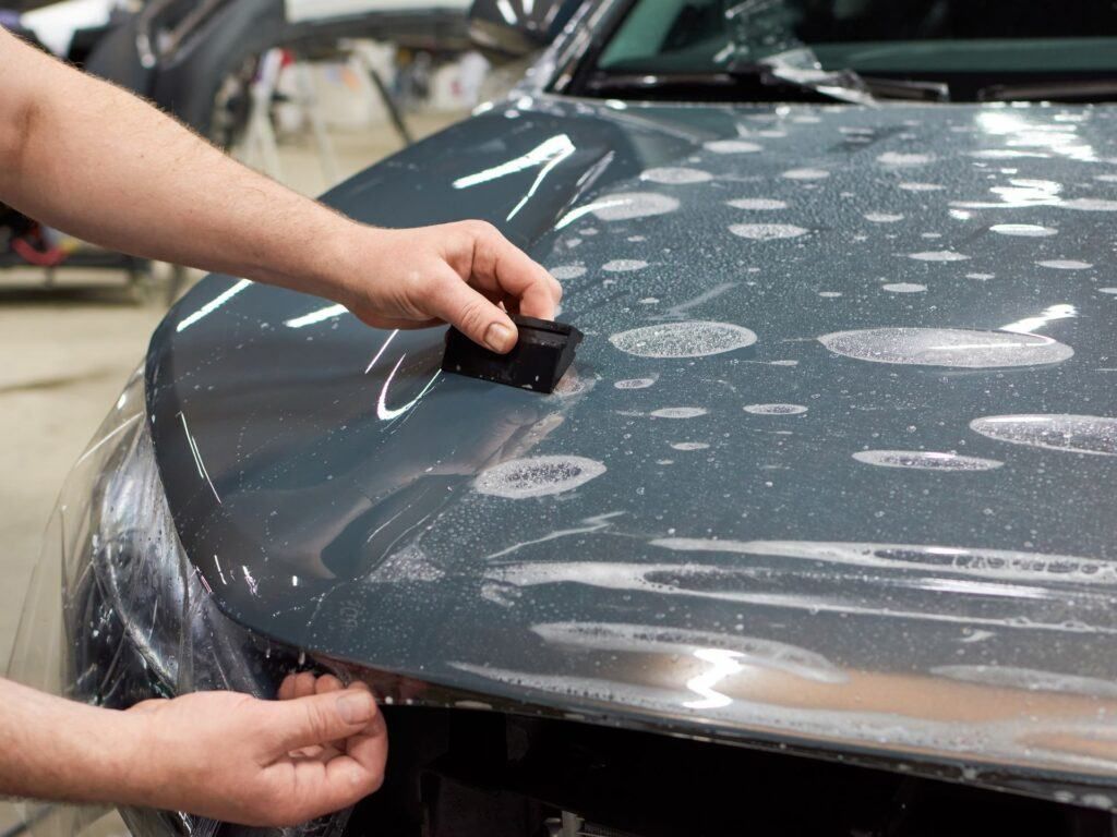 A man is applying a protective film to the hood of a car.