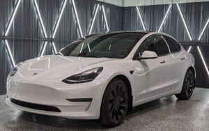 A white tesla model 3 is parked in a garage.