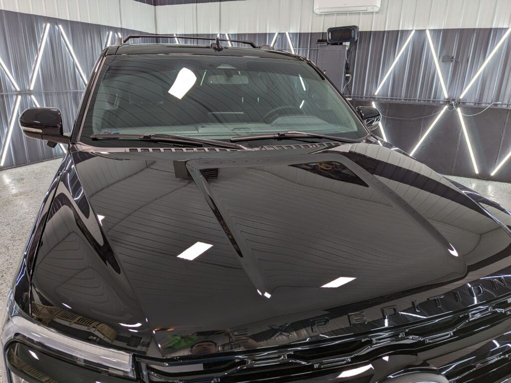 A black car is parked in a garage with the hood up.