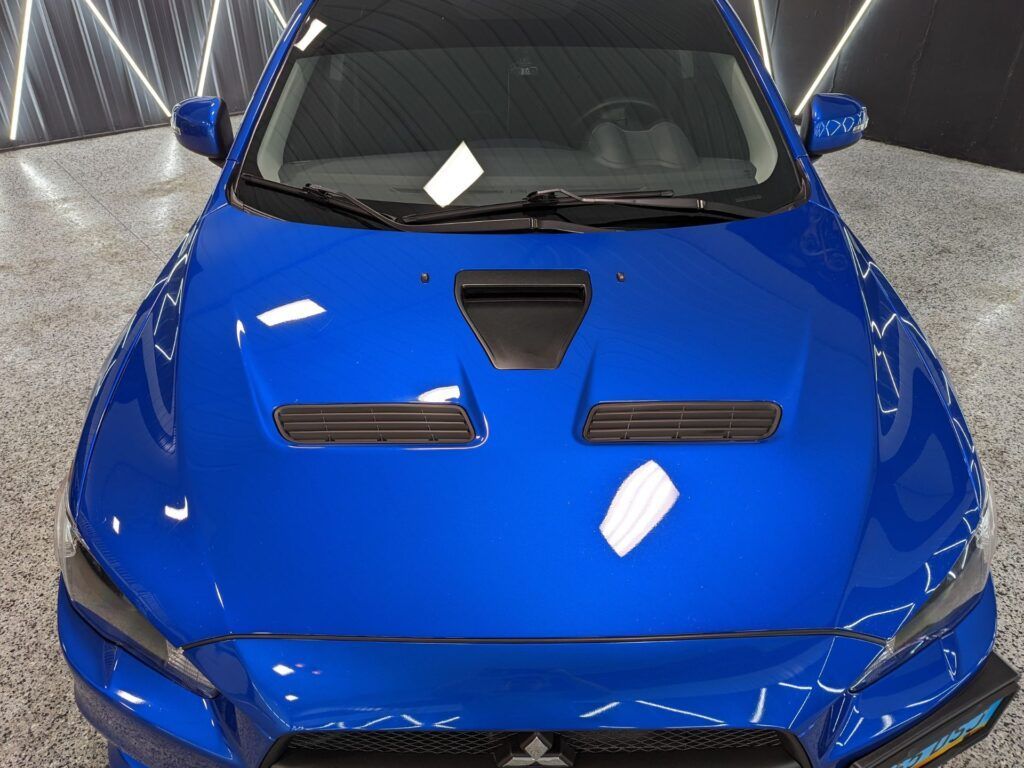 A blue car with a black hood is parked in a garage.